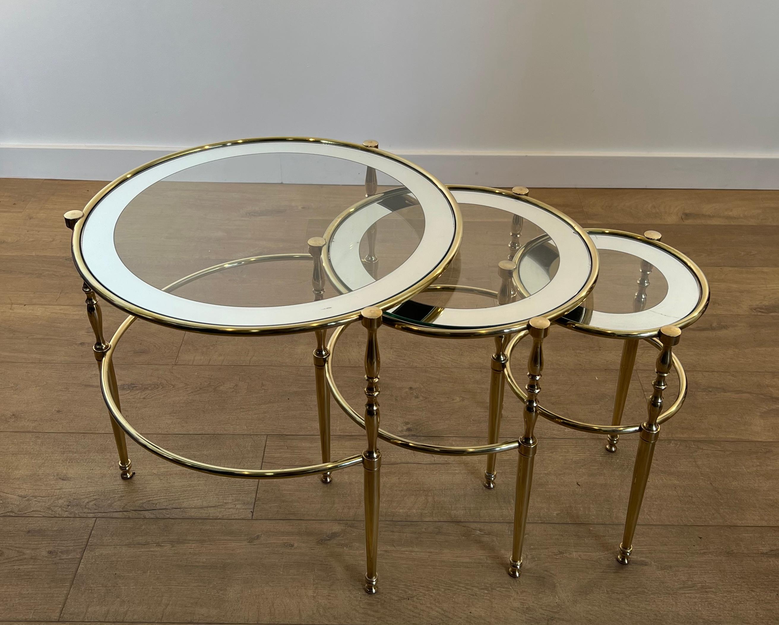 Ce très bel et élégant ensemble de 3 tables gigognes rondes est en laiton avec des plateaux en verre entourés de rebords argentés. Il s'agit d'un ouvrage français. Circa 1940