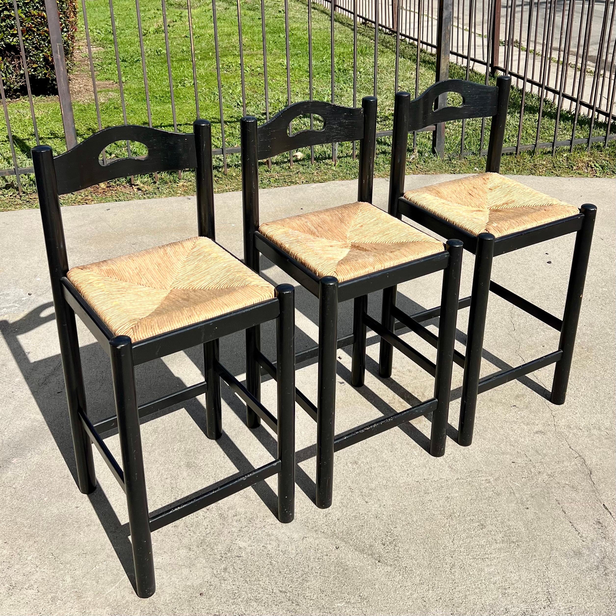 A set of vintage (c. 1990s) rush seat counter height stools in the manner of Hank Lowenstein’s Padova design. No markings. Black lacquer frames withs rush seats. Some cosmetic wear to seats and frames consistent with age and use. Please see detailed