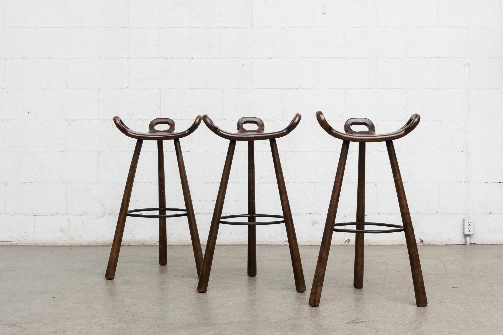 Set of 3 lightly refinished Spanish brutalist bar stools by Sergio Rodriguez. Dark oak frames with black enameled metal circular foot rests. Wear consistent with age and usage. Set price.