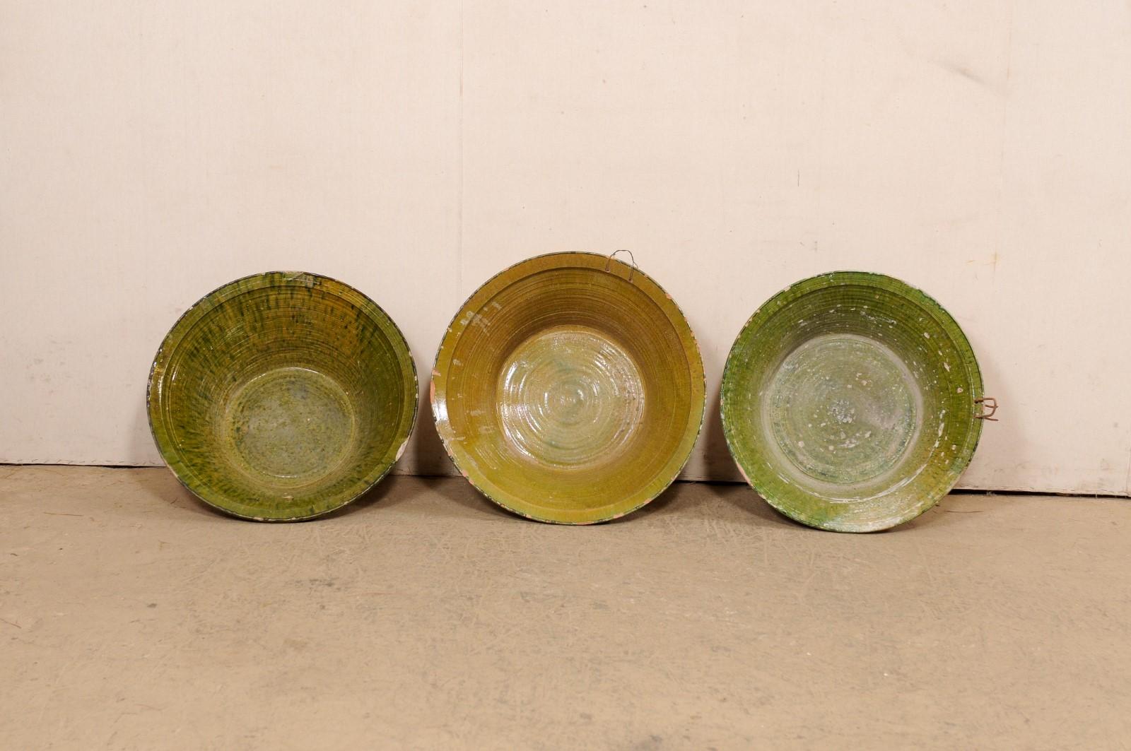 A Spanish set of three glazed terracotta bowls from the early 20th century. This collection of antique bowls from Spain are each round in shape, with widest part being at the top lip, and gradually tapering down and resting upon a flat base. There