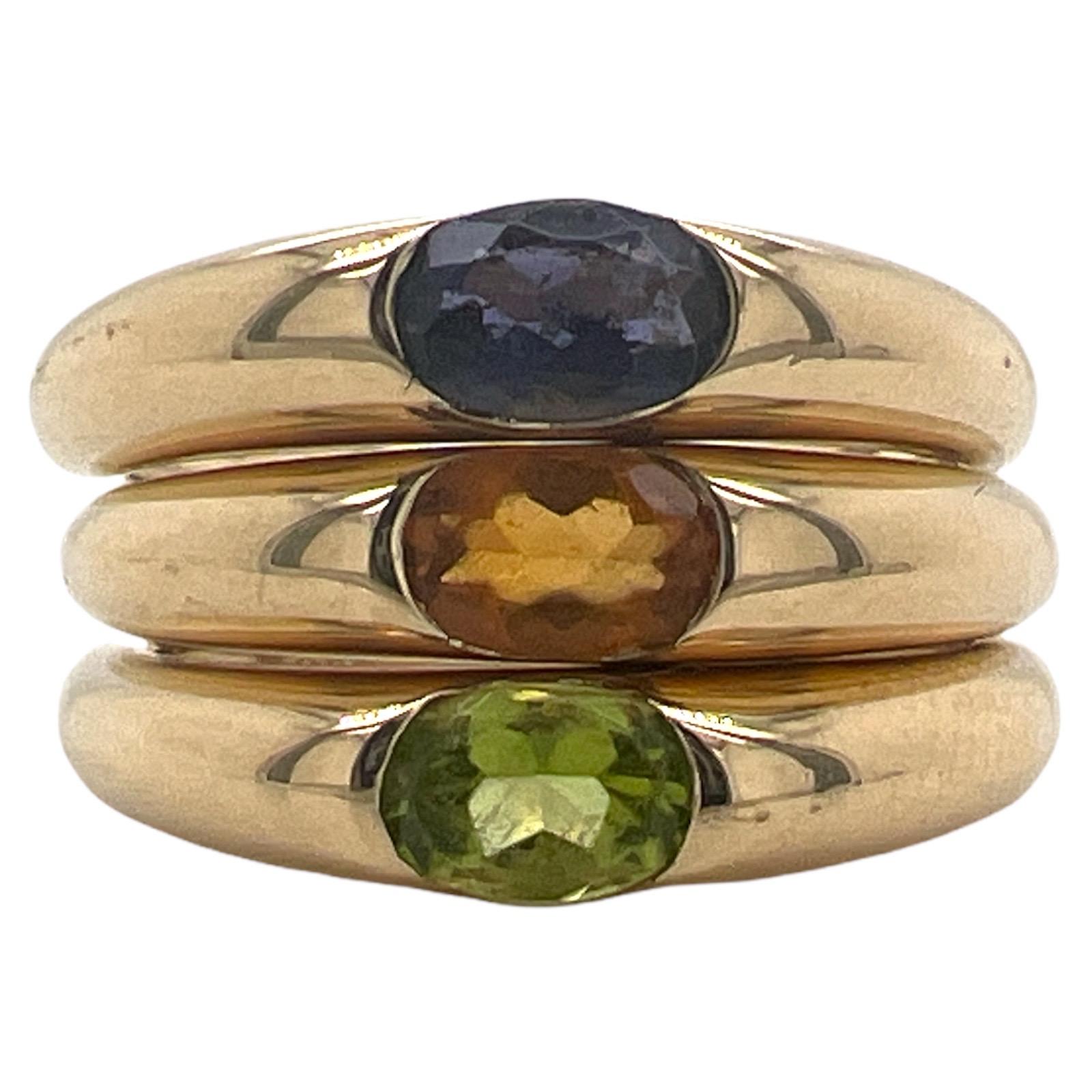 Set of three stacking bands fashioned in 18 karat yellow gold. The bands feature bezel set iolite, citrine, and peridot gemstones. The bands each measure 4mm in width, and are currently size 6.75 (can be sized). 