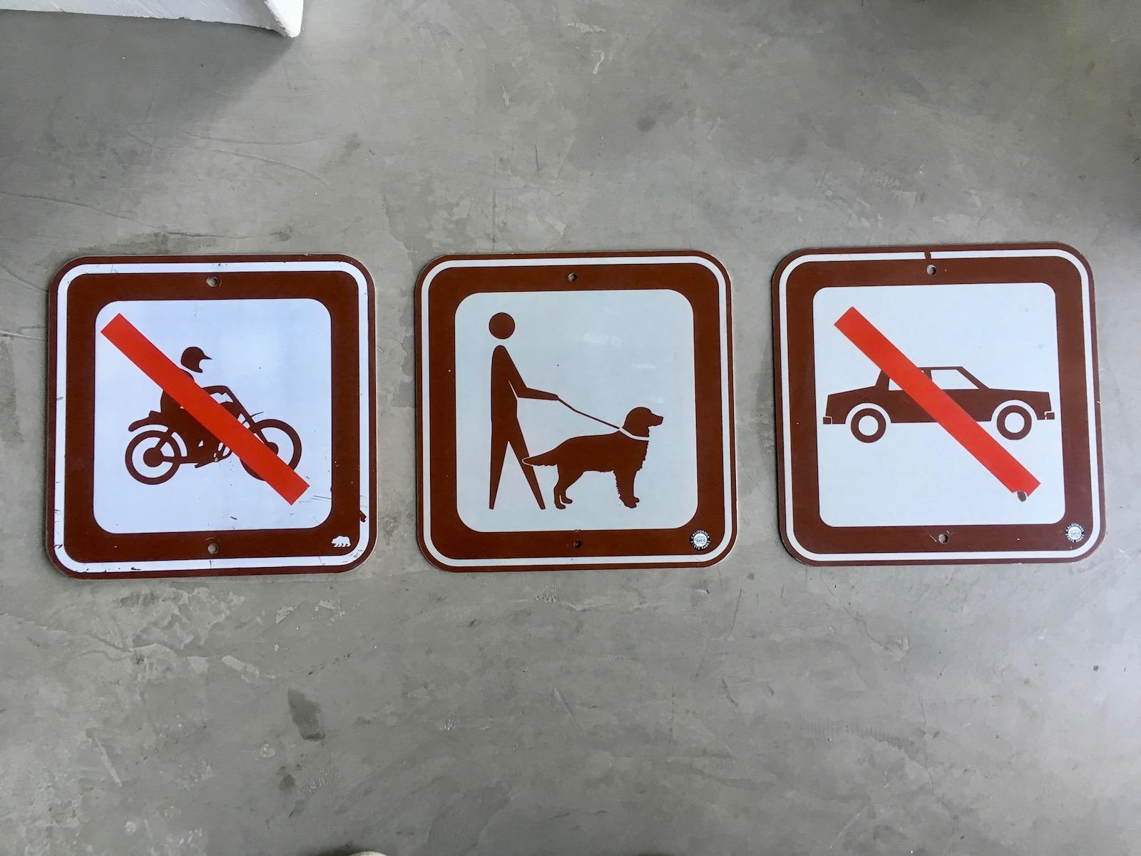 Cool triptych of three vintage signs from a California State Park. First sign is a no motorcyclist’s sign. The second is a dog walking sign. And the last is a no motorists sign. Bear logo on bottom right of motorcyclists sign. Bear logo with