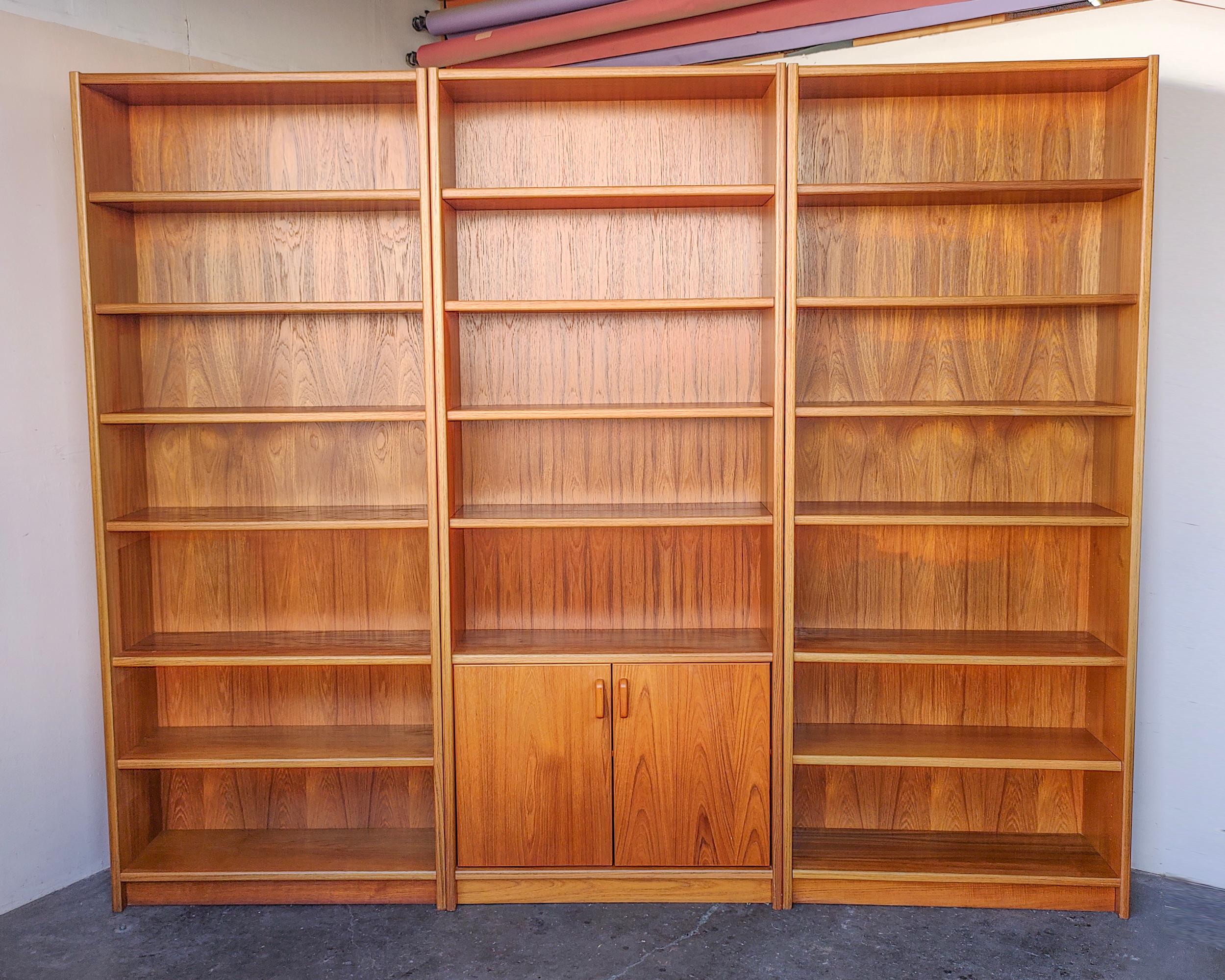 Set of three Danish modern teak bookshelves featuring a matching pair with six shelves on each and a third shelf with cabinet. Adjustable shelves except one fixed in the center. Sun fading on interior surfaces and shelves which would be made more