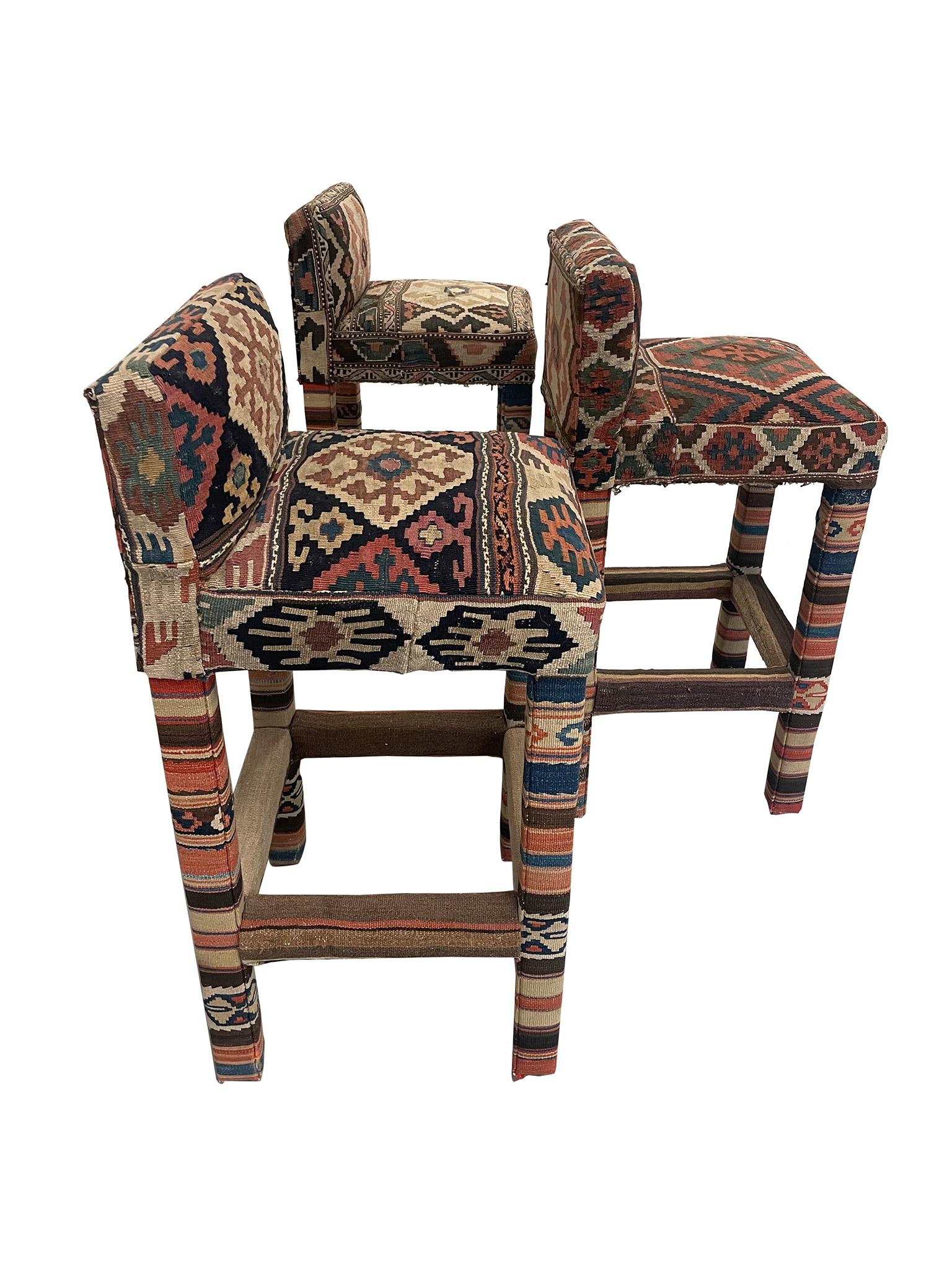 Lovely and contemporary set of three counter or bar stools in the style of George Smith, upholstered in Turkish Kilim fabric. Each of the three stools features a collage of different Kilim fabric in complementing reds, blues, and tans. The