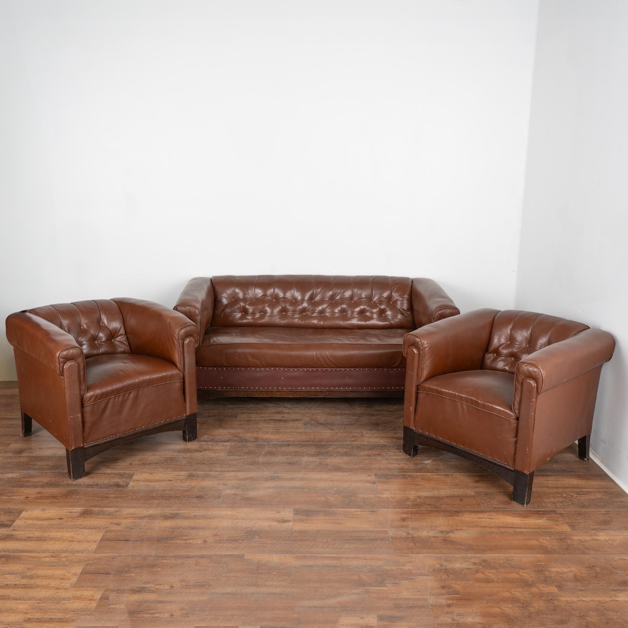Ensemble (3) canapé vintage en cuir marron et paire de fauteuils club.
Vendu dans son état d'origine. Le cuir marron présente des éraflures, des rayures, des boutons manquants/récupérés, des impressions, le cuir sur le devant du canapé a été