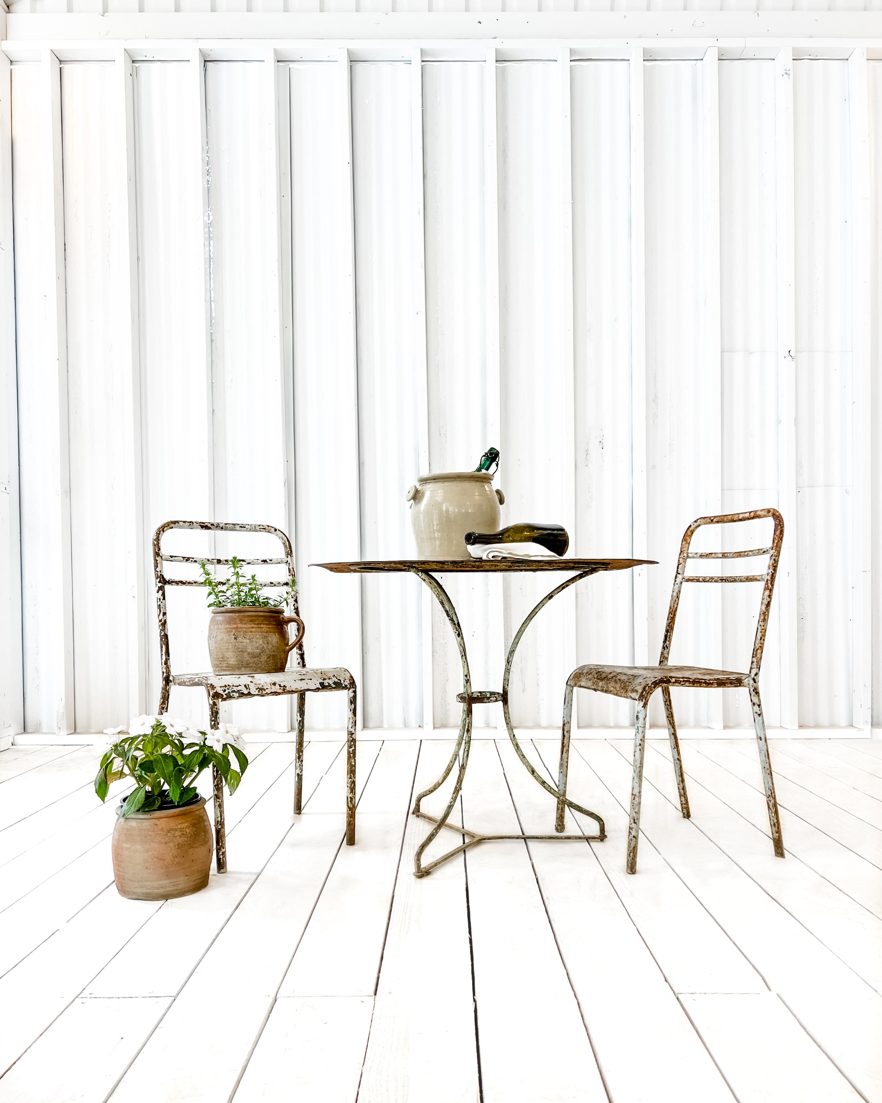 Charming metal bistro table with two matching chairs. Worn by the elements and showing myriad chippy paint layers, the set has acquired a wonderful patina. Simple and unassuming in design, both the table and chairs feature soft curves which are