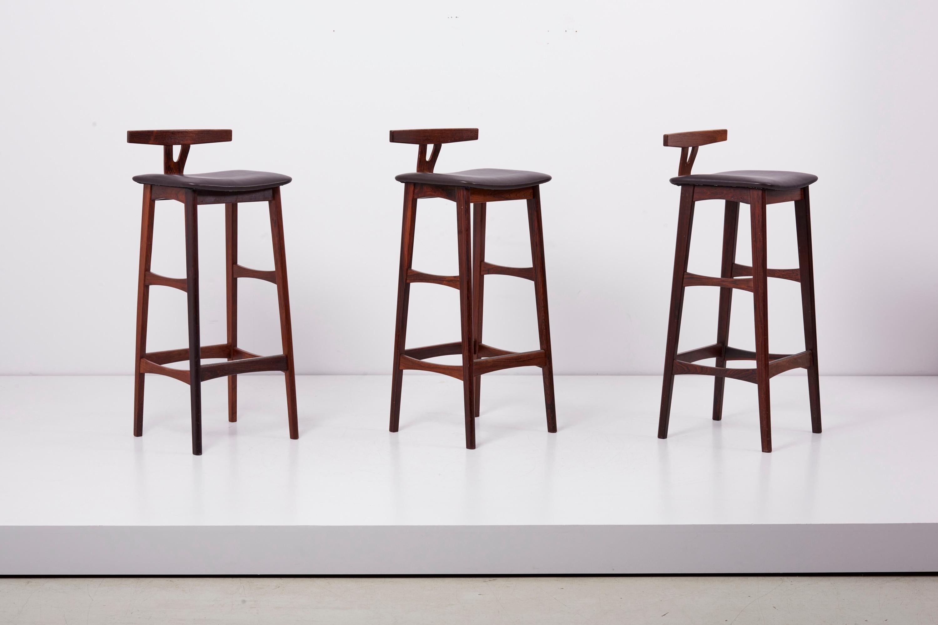 Set of three barstools with low T back, designed by Erik Buch in 1960s and manufactured by Dyrlund in Denmark (labeled). Made of wood / plywood and professionally reupholstered in matching dark brown Sorensen leather - great condition.