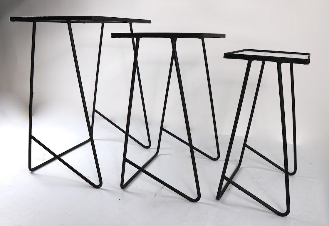Nice set of three graduated size wrought iron nesting tables, with glass tops. Stylish architectural design, recently repainted in semi gloss black finish, with new glass tops, suitable for both indoor and outdoor use.
Design reminiscent of McCobb,