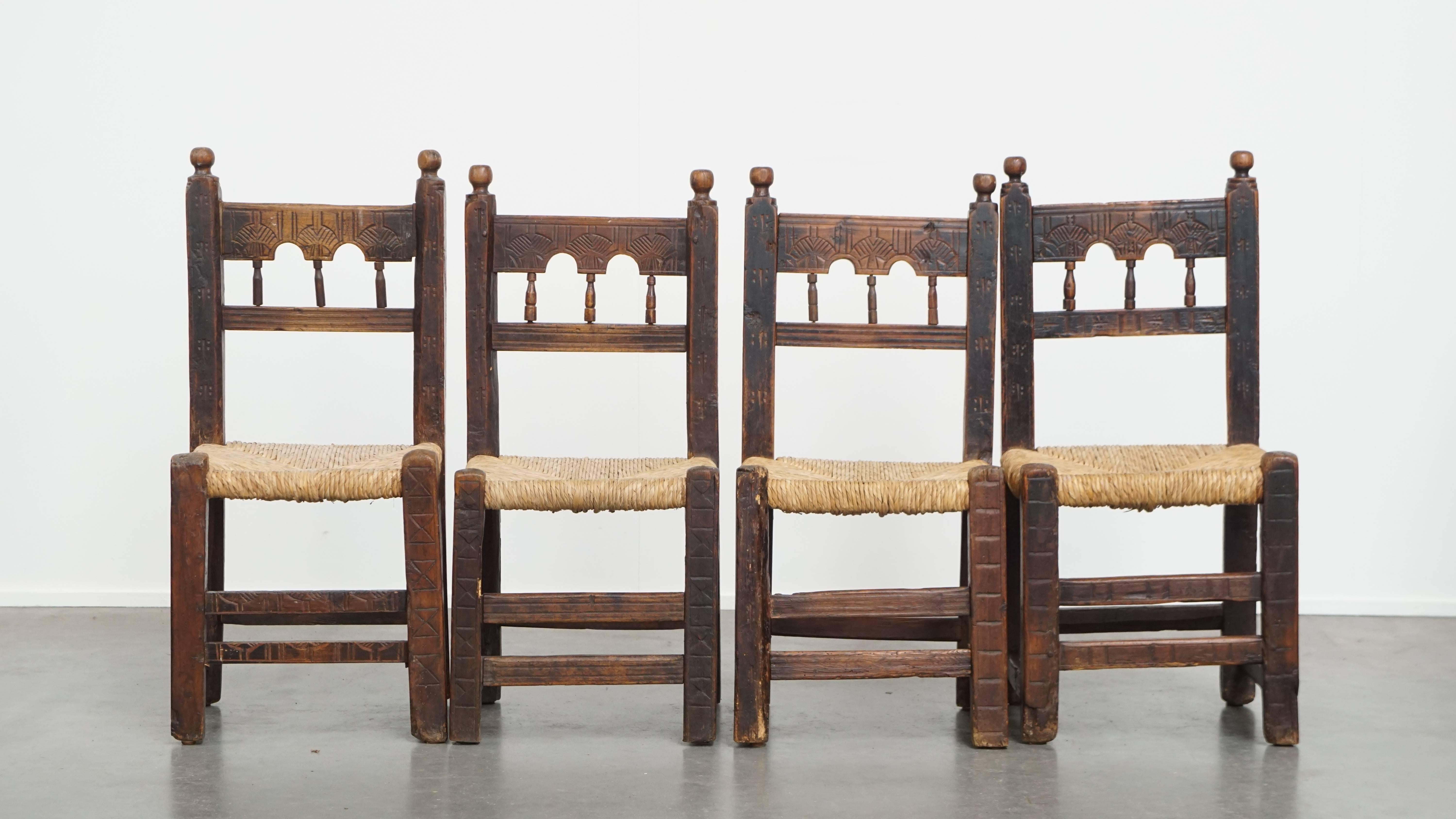 Offered: this unique set of 4 antique Spanish country chairs with woven rattan seats and beautiful wood carvings. This charming set of 4 antique Spanish country chairs is not only visually appealing but also highly versatile. They can be used as