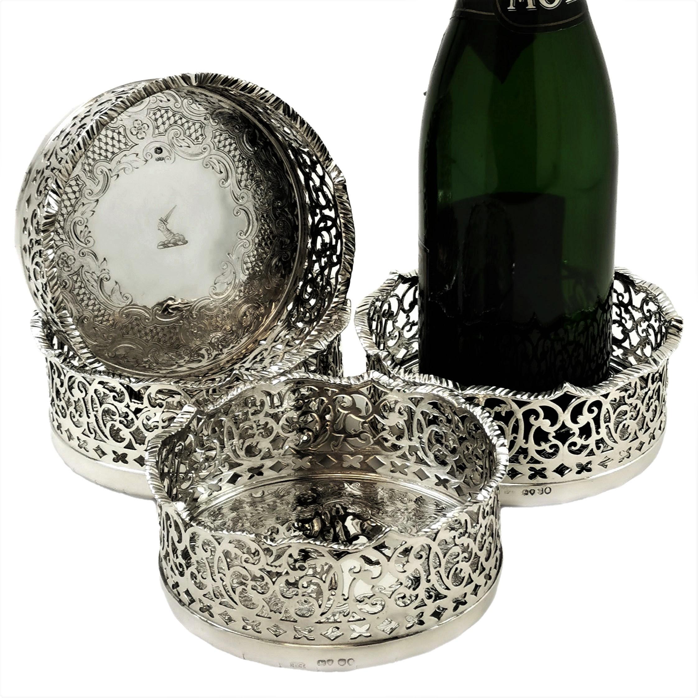 A magnificent set of four Antique Solid Silver Bottle Coasters. Each Coaster has a tall, ornate pierced sides with a shaped rim. The interior of each Coaster is decorated with a delicate complementary engraved design around an engraved crest. These