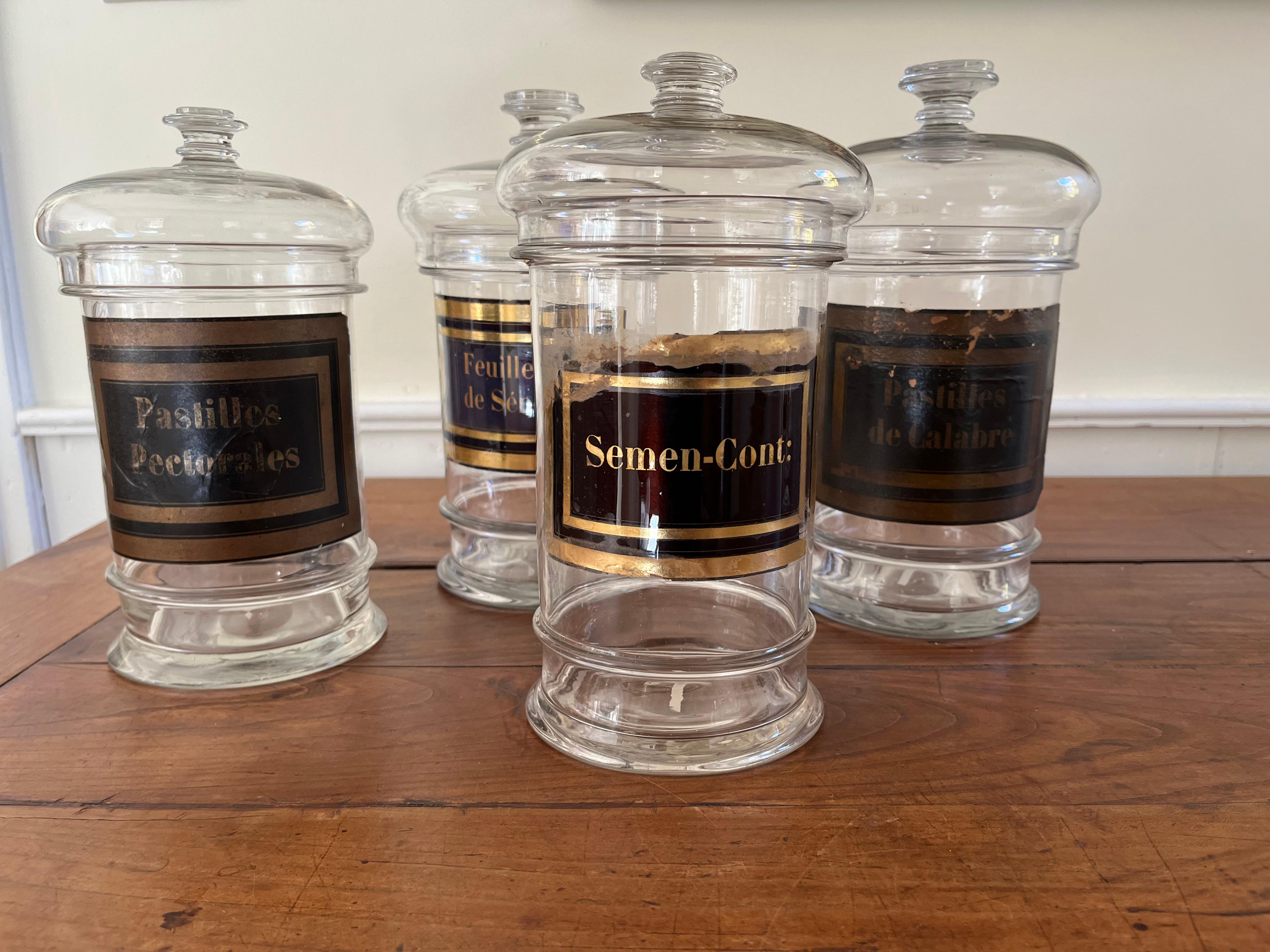 A set of 4 mid-19th century apothecary jars with lids, hand-blown with paper labels and polished pontil marks on the base.