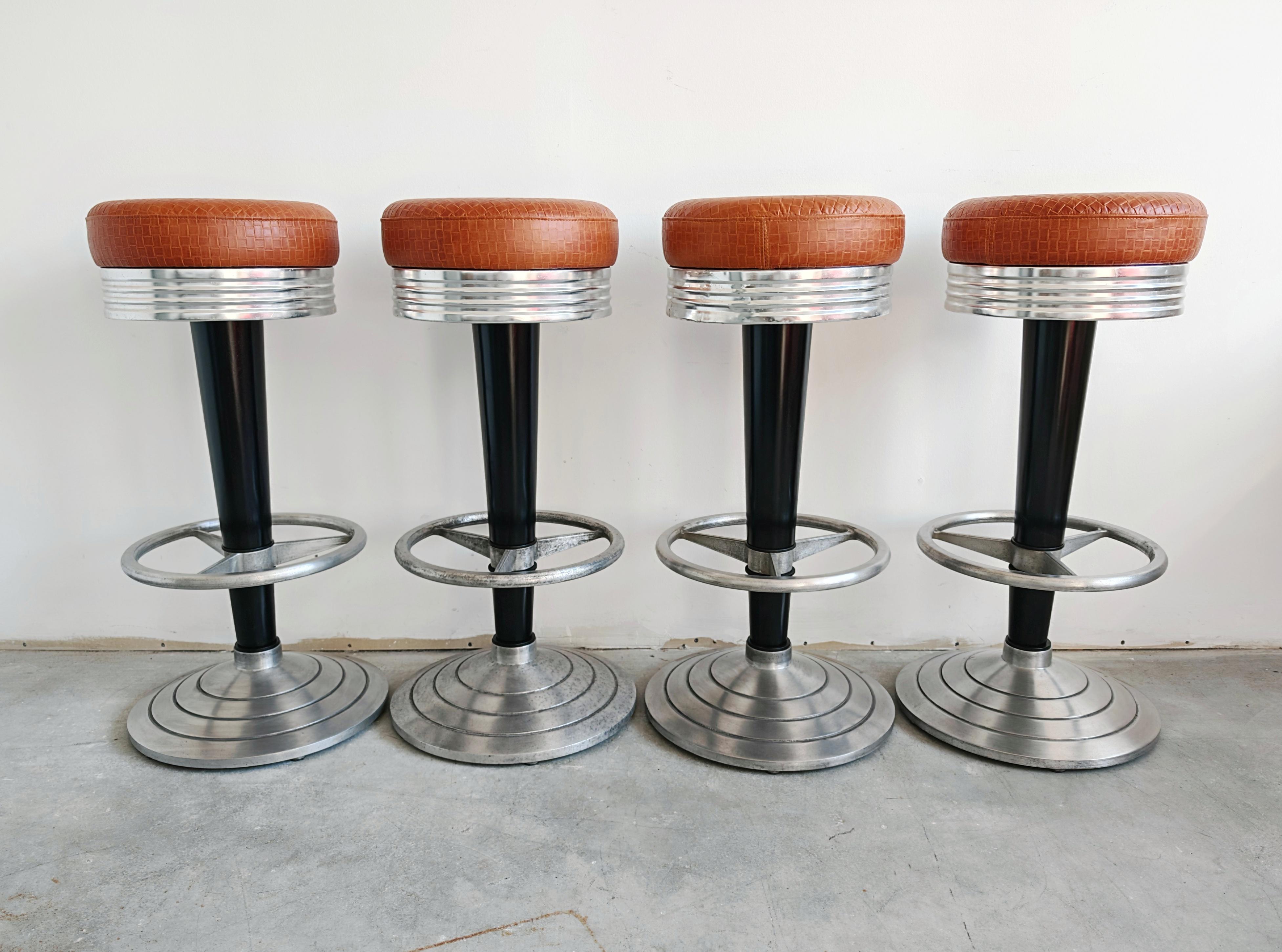In questo annuncio troverai un set di 4 sgabelli da bar di ispirazione Art Deco. Sono realizzati in fusione di alluminio e legno e rivestiti in pelle naturale cognac con rilievo a rete. Prodotto da Go-In Design Munich, con l'etichetta del produttore