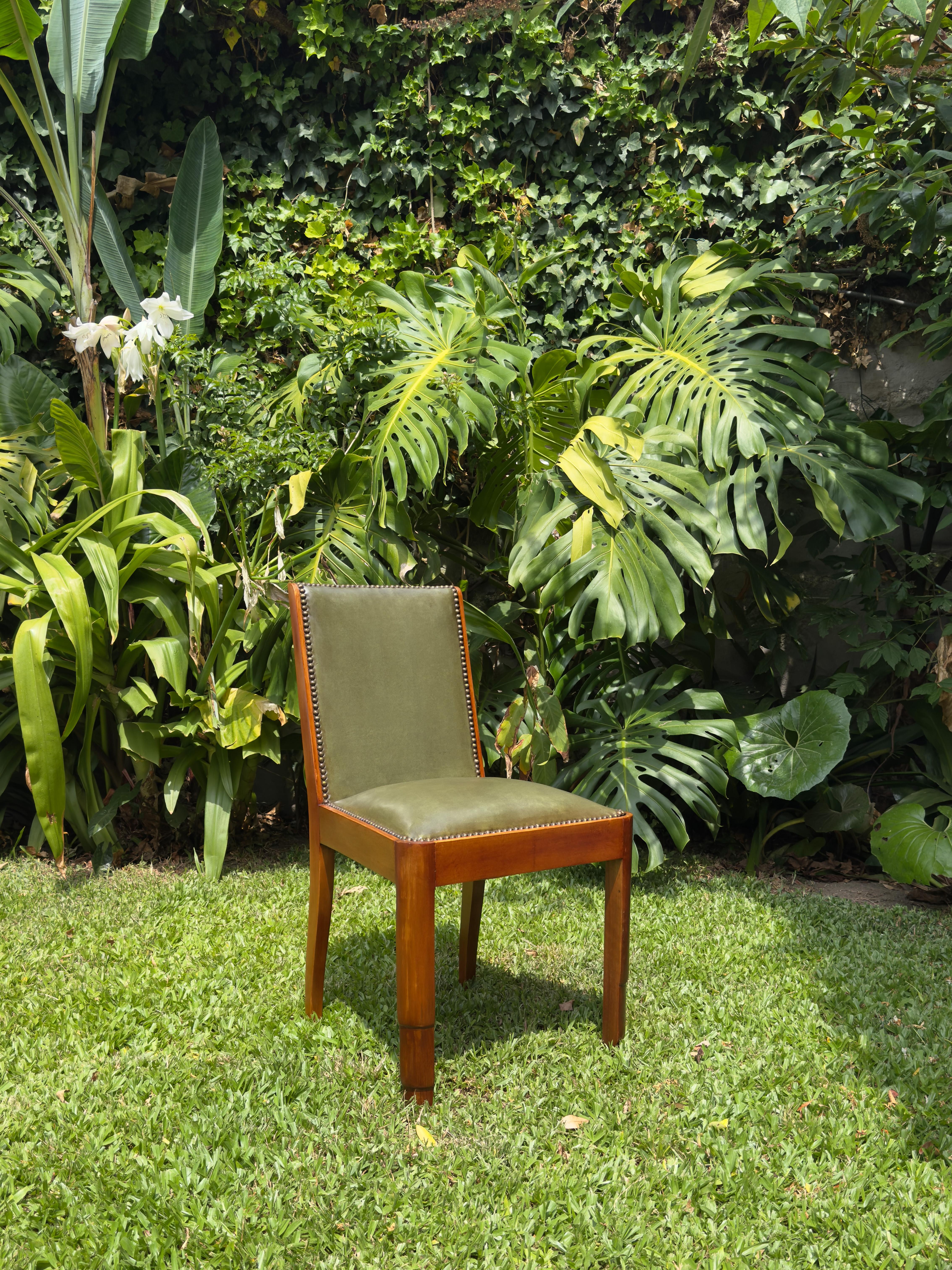 This set of four of Art Deco chairs from the 1920s features green upholstery and solid wood frames. 
With their clean lines and brass nailhead trim, these chairs embody the refined geometric spirit of the era. 
The rich walnut wood adds warmth and