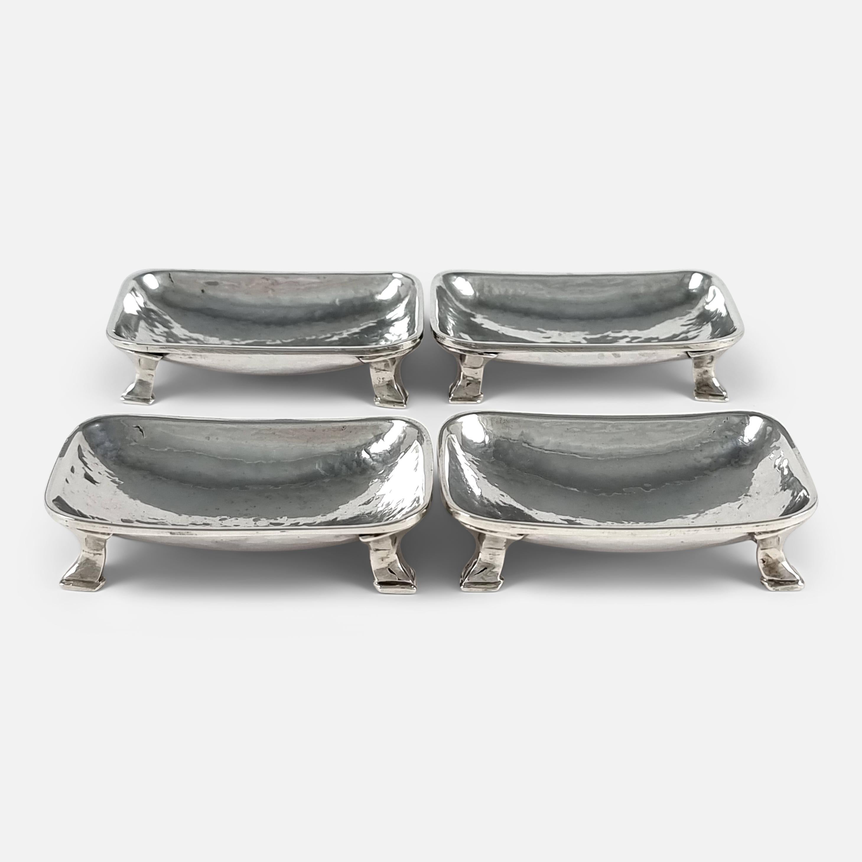 A set of 4 Arts and Crafts sterling silver salts by Omar Ramsden, 1935. The salts are of rectangular outline, the hammered silver bowls raised on four swept feet. They are stored in the original wooden case, the inside of the hinged cover written on