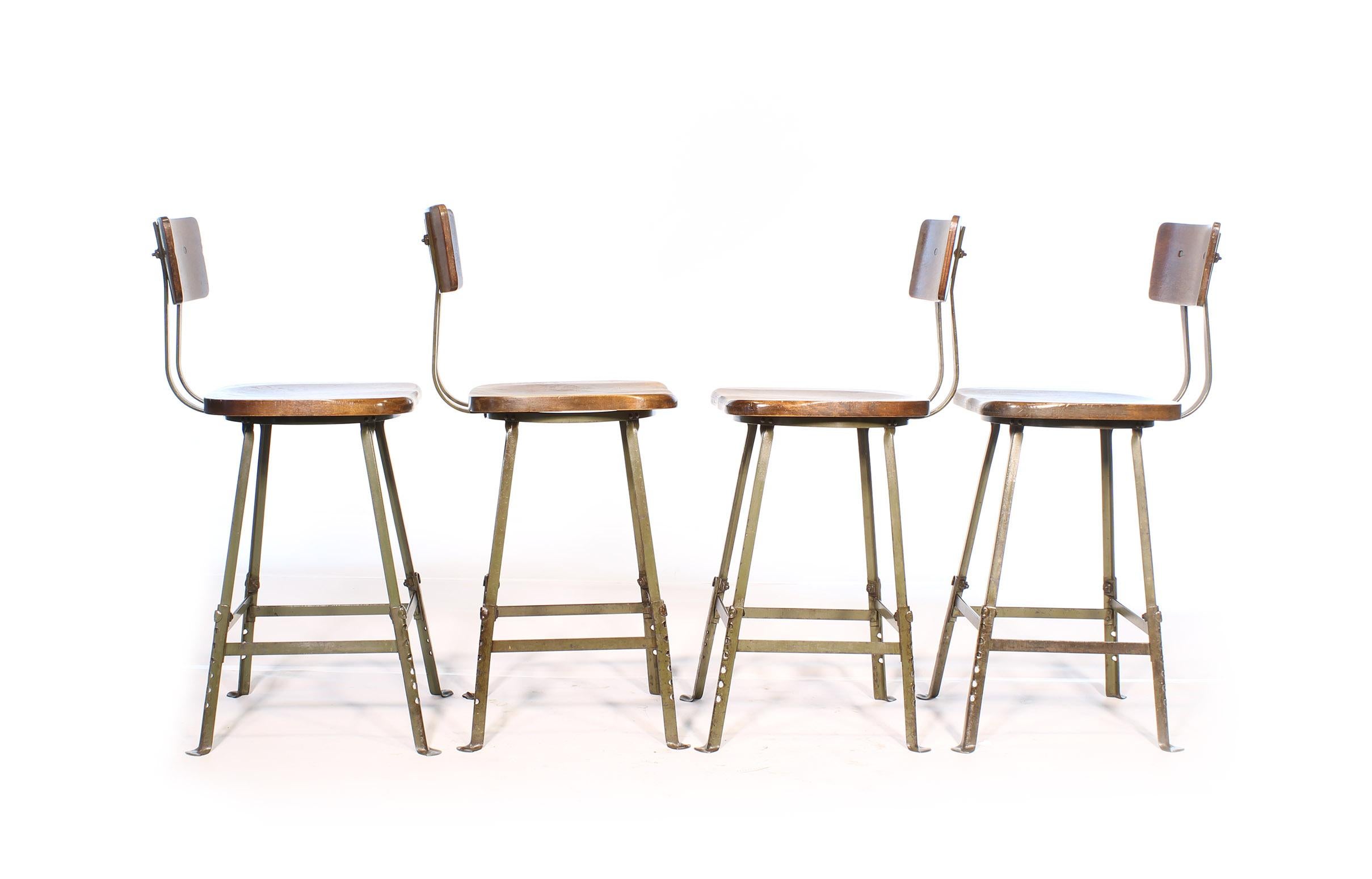 Authentic set of four vintage Industrial factory / shop stools. Feature adjustable steel bases, formed solid wooden seat and solid wood height adjustable backrest. Stools have been cleaned and checked for stability, and adjusted to their maximum