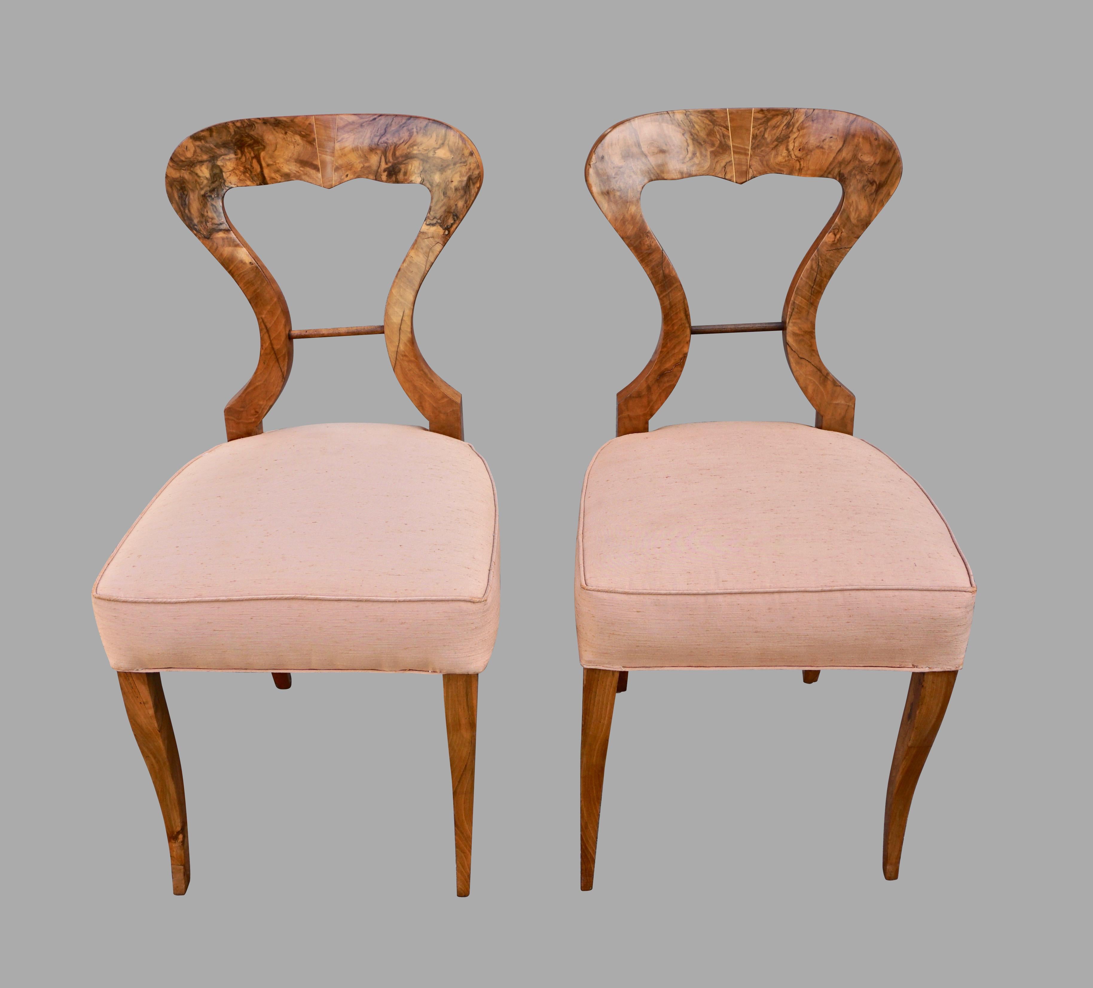 A set of 4 Austrian or Northern European walnut upholstered side chairs with curved backs centered with an inlaid detail, the upholstered seat supported on curved legs. Circa 1830.