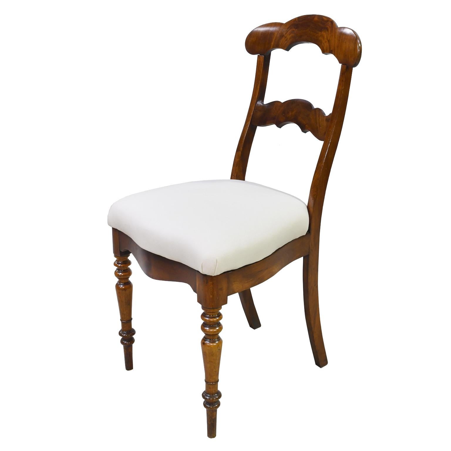 A set of 4 Biedermeier dining chairs in West Indies mahogany with upholstered slip seat. Back is high and has two cross rails with scrolled arches featuring a beautiful crotch mahogany. Seat has a serpentine front and sides with inverted arches on