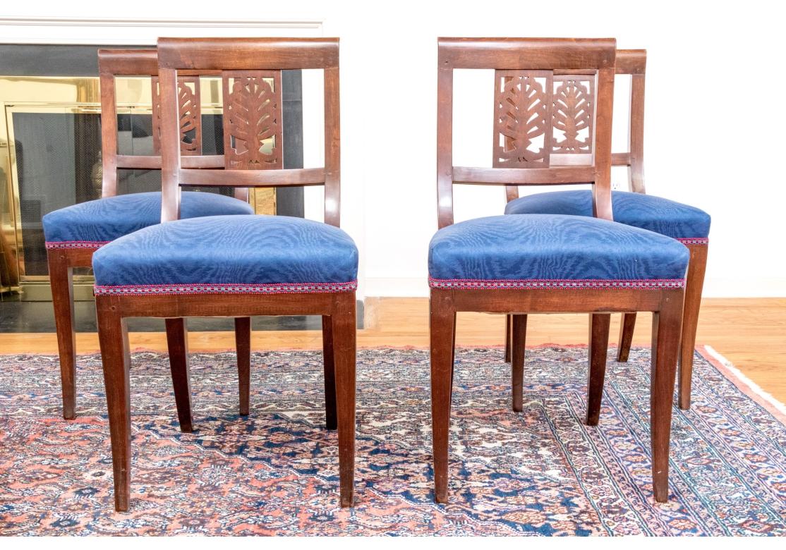 Ensemble de quatre chaises de salle à manger en acajou avec construction à ressorts et bobines, sièges rembourrés en bleu avec garnitures multicolores. Les chaises ont un dossier percé et l'ensemble repose sur des pieds légèrement évasés. Chaises
