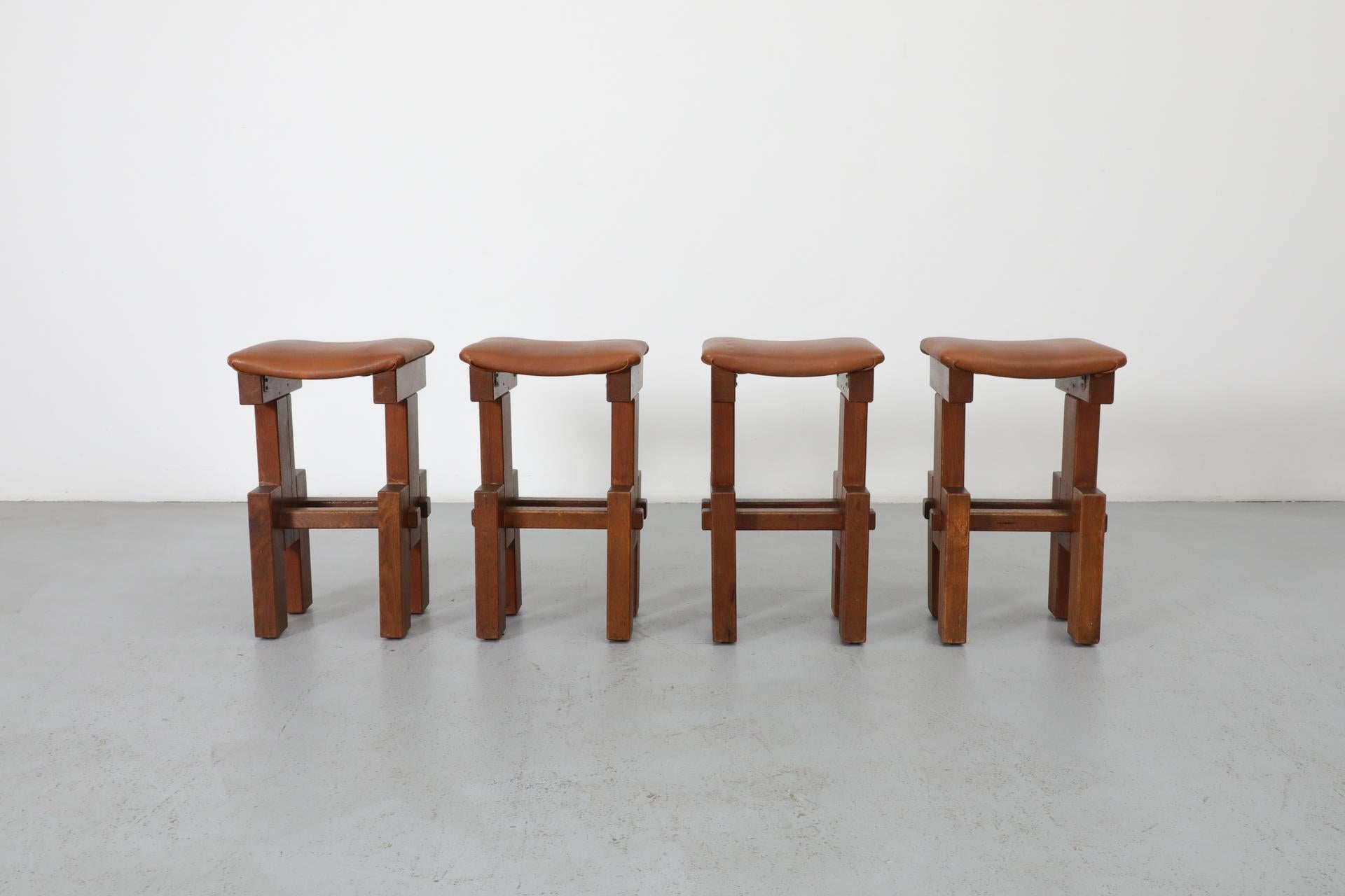 Set of 4 solid dark oak Brutalist counter stools with a unique architectural silhouette, 1970s. Handsome and eye catching Brutalist design. The stools are outfitted with brown leatherette seats. Legs and seats have been reinforced in past with metal
