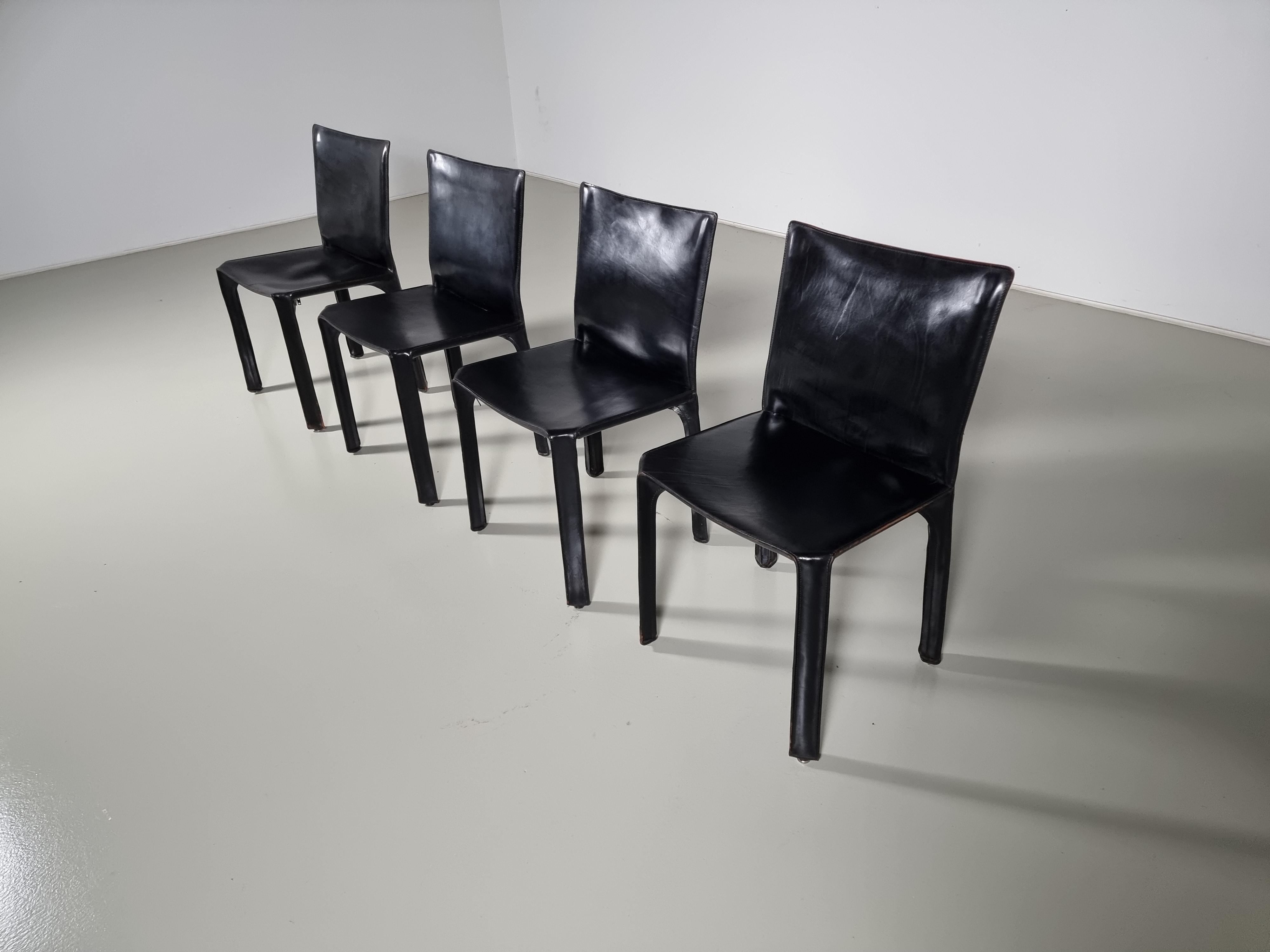 Set of 4 early edition CAB-412 dining room chairs in black saddle leather. Designed by Mario Bellini and manufactured by Cassina in the 1970s in Italy. The leather cover is stretched over a minimal tubular steel frame. The only additional