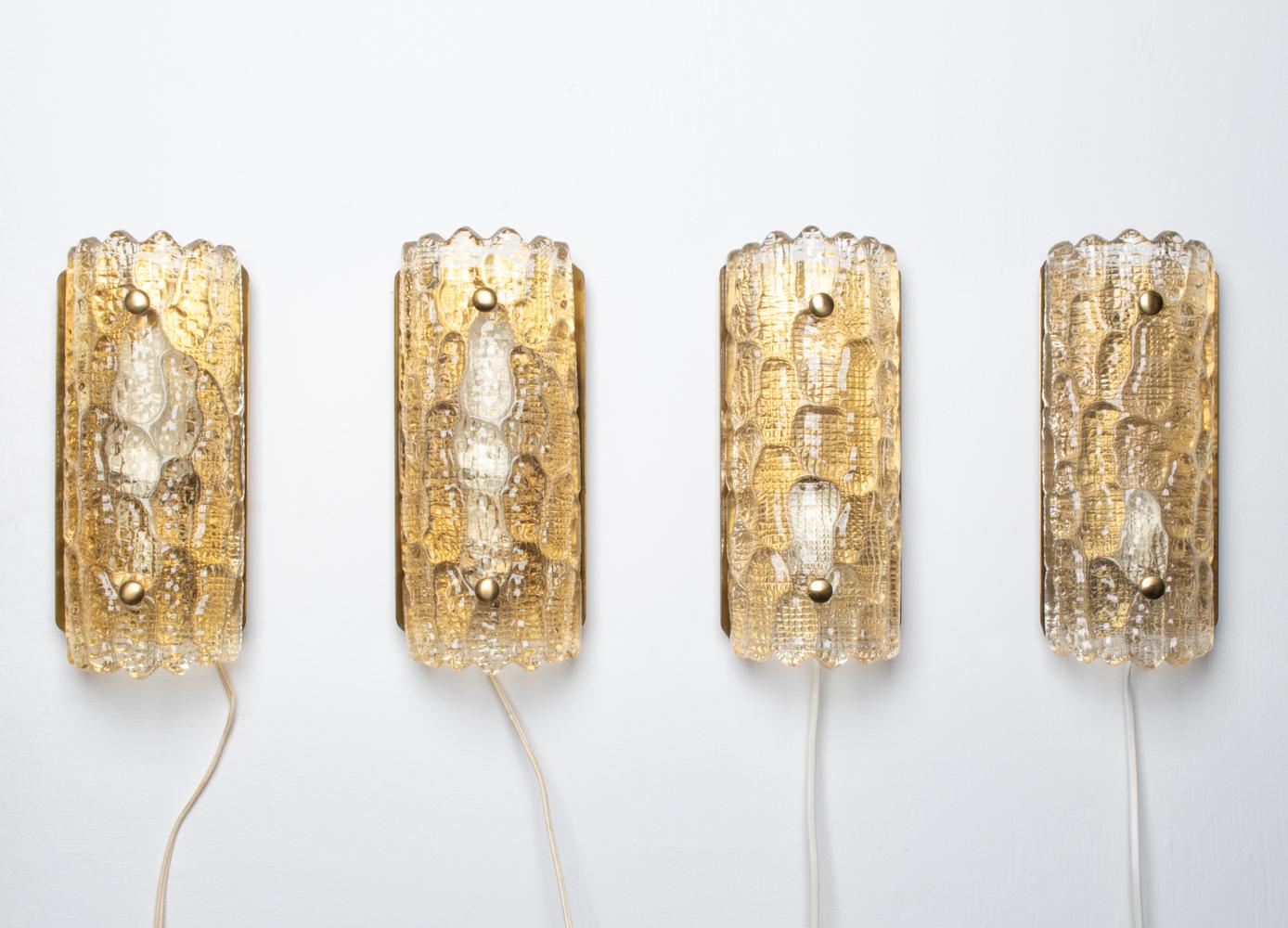 This exquisite set of (4) sconces was designed by Carl Fagerlund for Orrefors and produced in the 1960's. Each sconce features a single socket behind a curved pane of thick clear glass, molded with a pebbled ice floe texture on the front and an