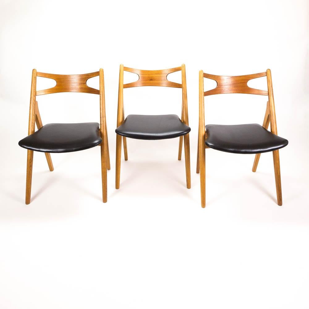 Set of 4 oak and teak framed CH29 Sawbuck dining chairs with new high quality black leather upholstered seats. 
Designed by Hans Wegner in the 1950s and made by Carl Hansen & Søn, Denmark, 1960s.