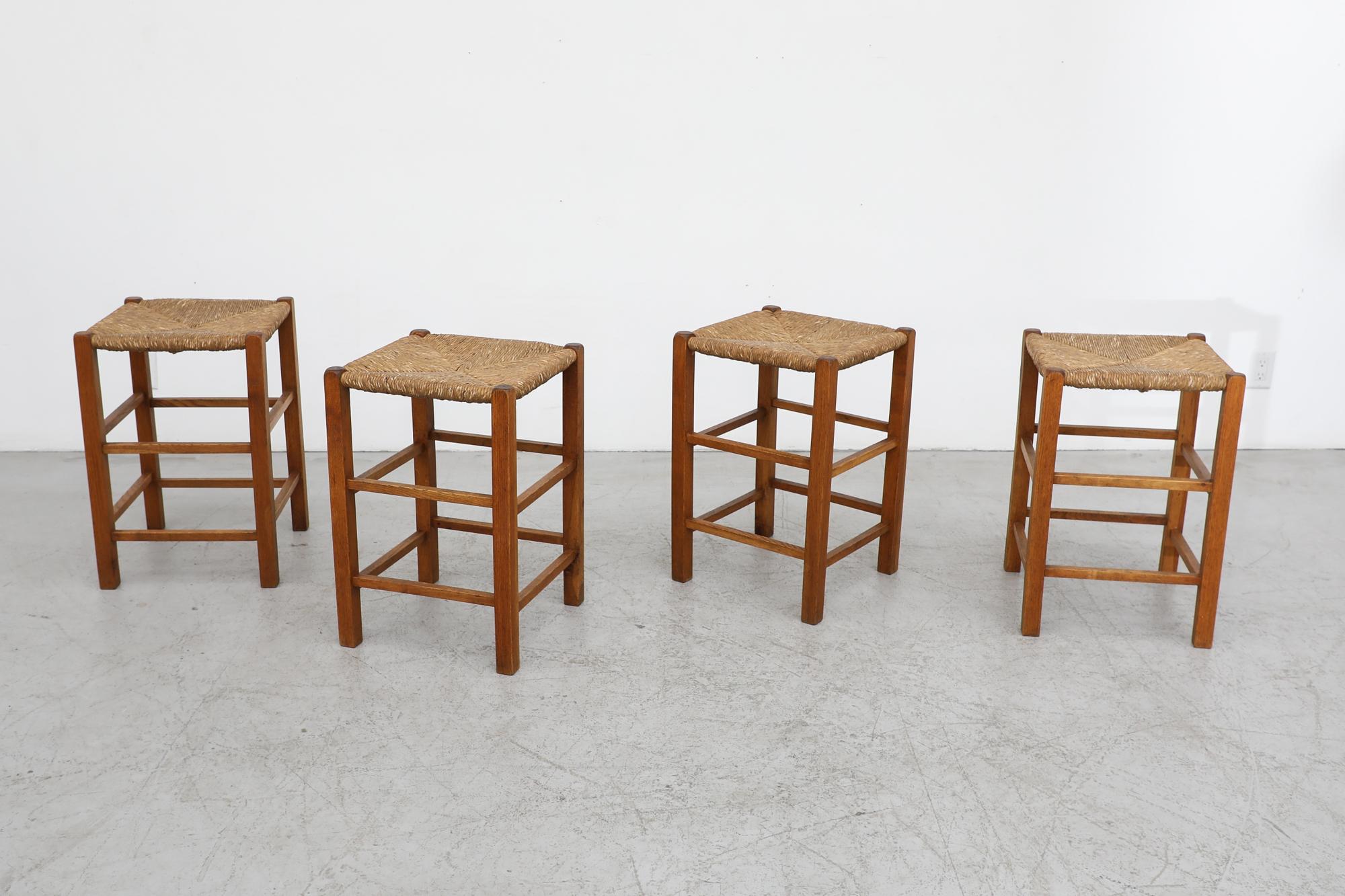 Handsome set of 4 Mid century Charlotte Perriand style counter stools with rush seats and oak frames. In original condition with visible wear and lovely patina. Wear is consistent with their age and use. Similar stools also available listed