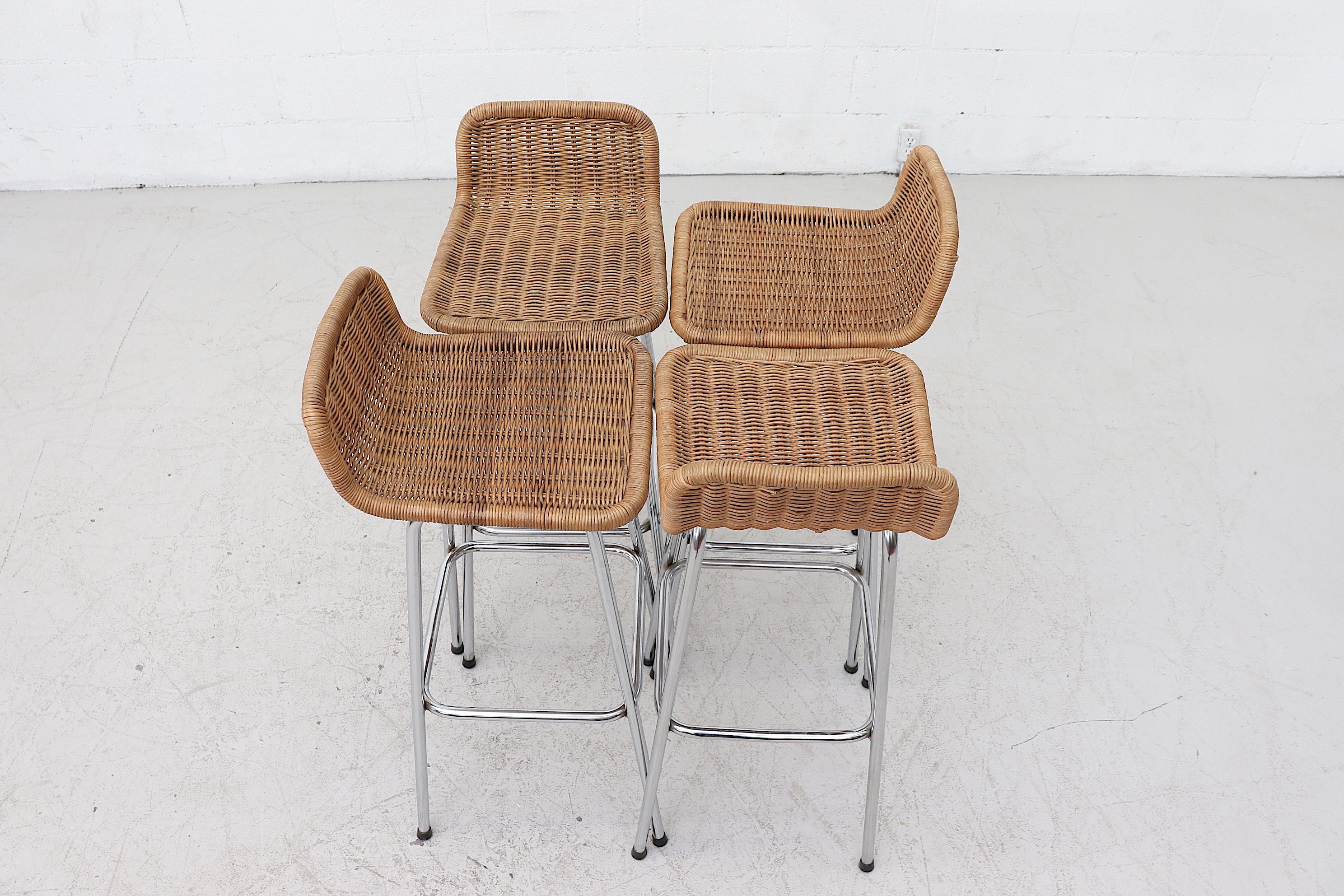 Set of 4 Charlotte Perriand style bar stools with low rounded rattan seat and chrome tubular frame in original condition with visible wear. Wear varies from stool to stool. Measures: Seat heights are 31