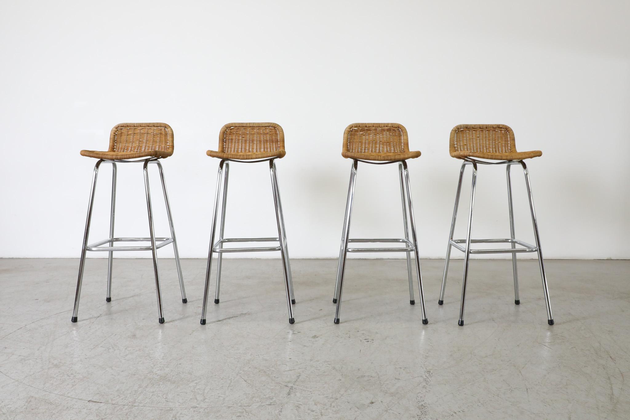 Set of 4 Charlotte Perriand style bar stools with low rounded rattan seat backs and chrome tubular frames. In original condition with visible wear consistent with their age and use. Wear and rattan color varies from stool to stool. Seat heights