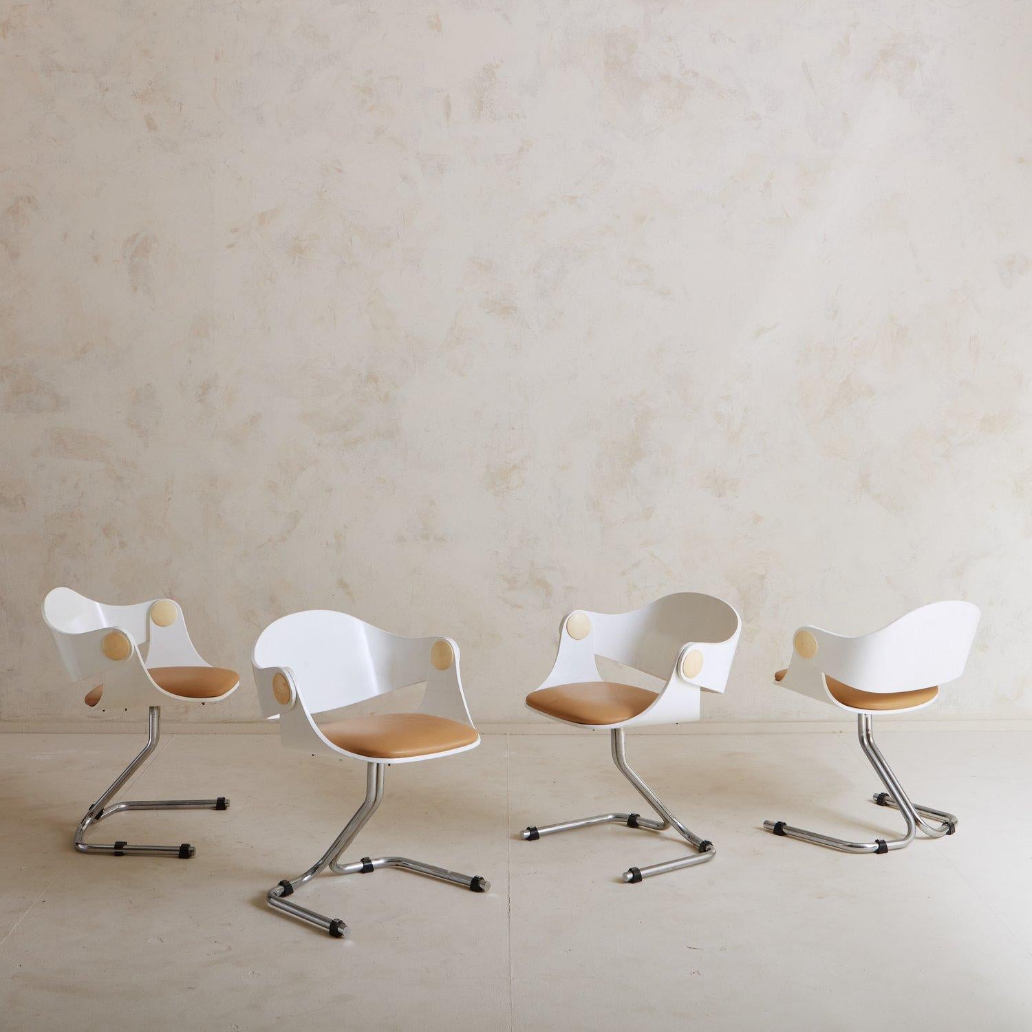 A set of four 1960s dining chairs attributed to Eugen Schmidt for Soloform. These chairs have white wooden frames with taupe leather seats. The backs attach to the bases at the arm with a taupe circular detail. These sculptural chairs feature