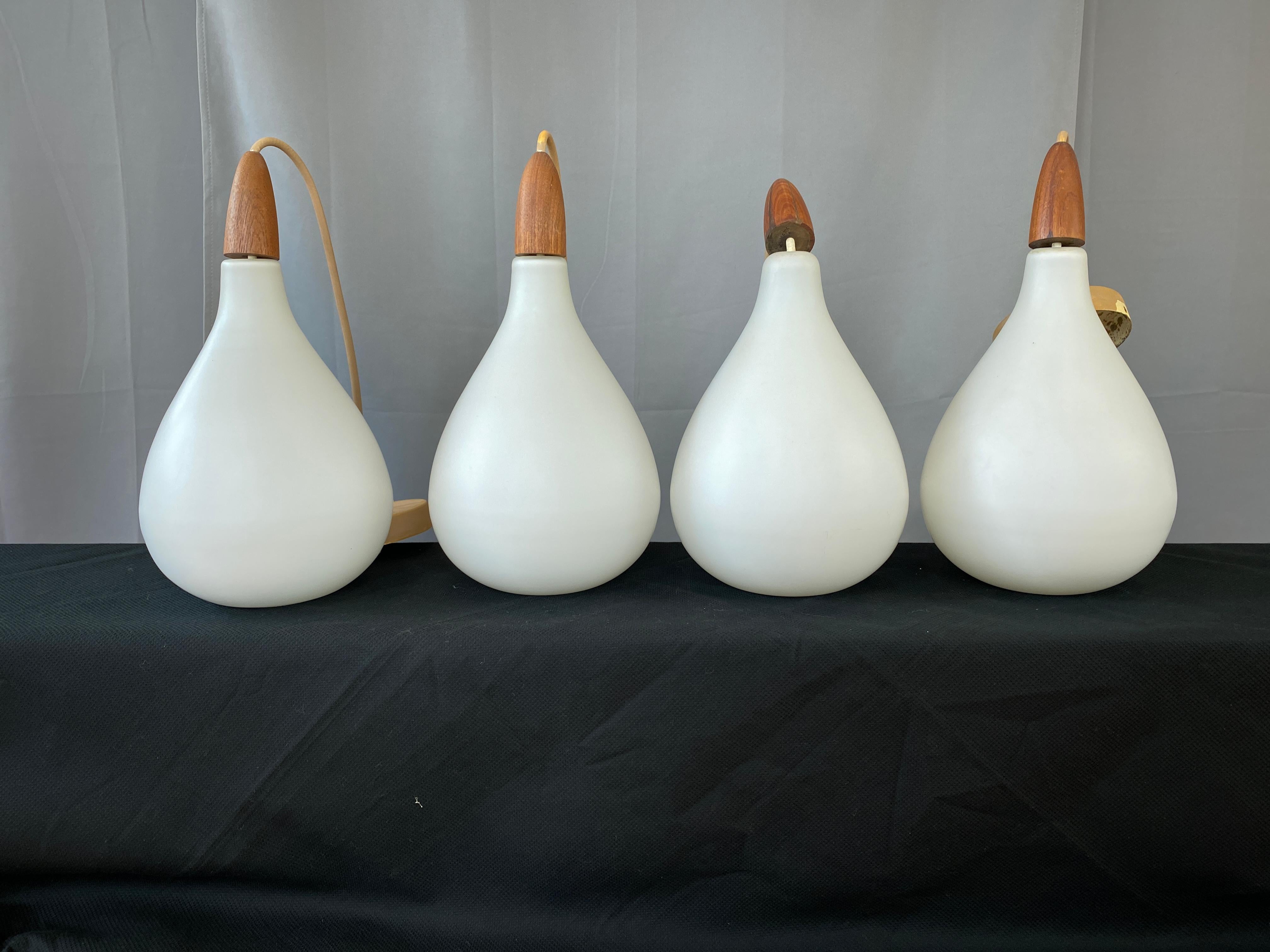 A nice set of 4 Danish white cased glass pendants with each one topped off with a solid teak finial.
The finial's have Denmark stamped on their underside. 
We are dating these from the 1960s.