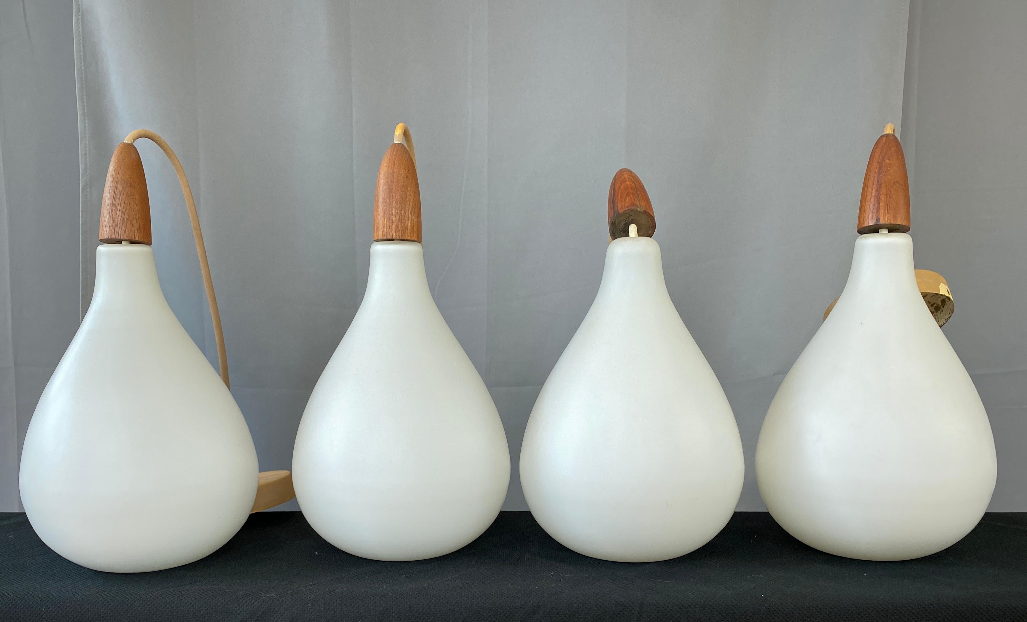 A nice set of 4 Danish white cased glass pendants with each one topped off with a solid Teak finial.
The finial's have Denmark stamped on their underside. We are dating these from the 1960s.