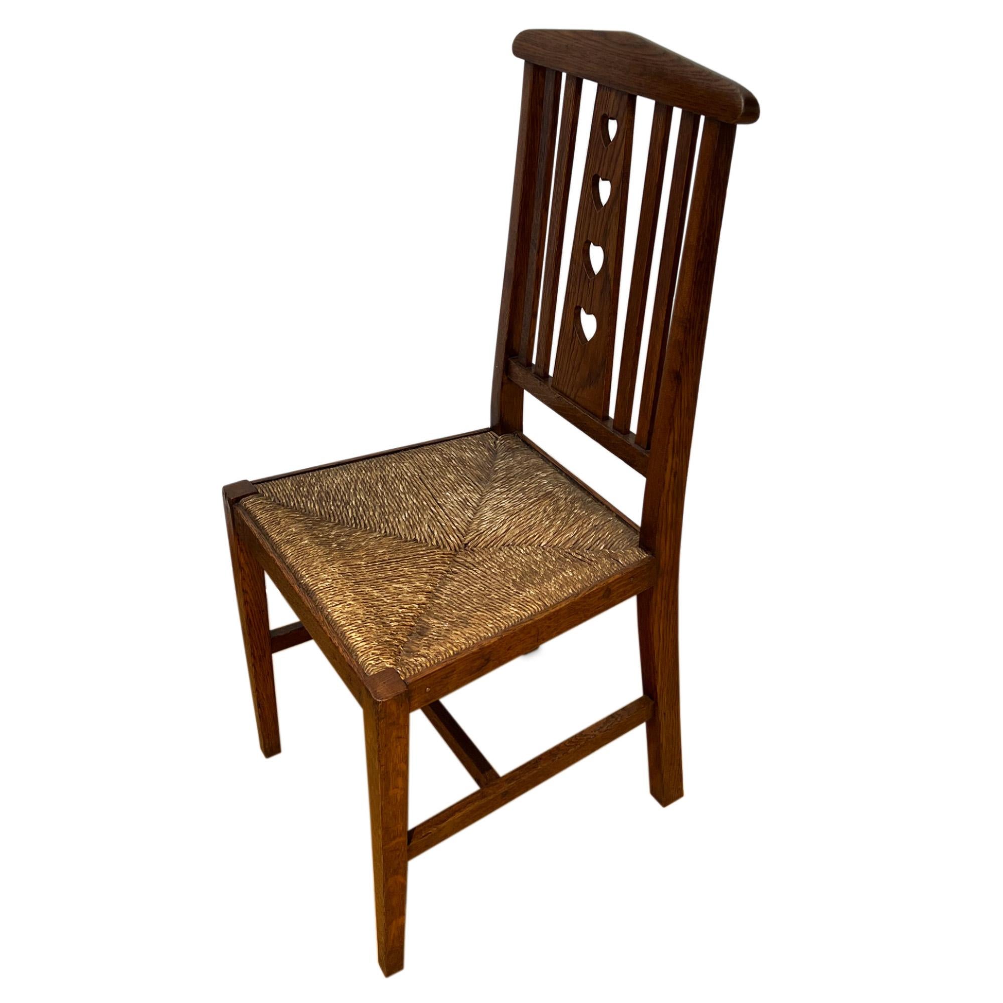 This is a set of four hall or dining chairs, which can also be sold in pairs. Price shown is for a set of two. 

Made from oak with a rush seat and a charming heart cut out detail. A great example of British Arts and Craft design. 

Seat height