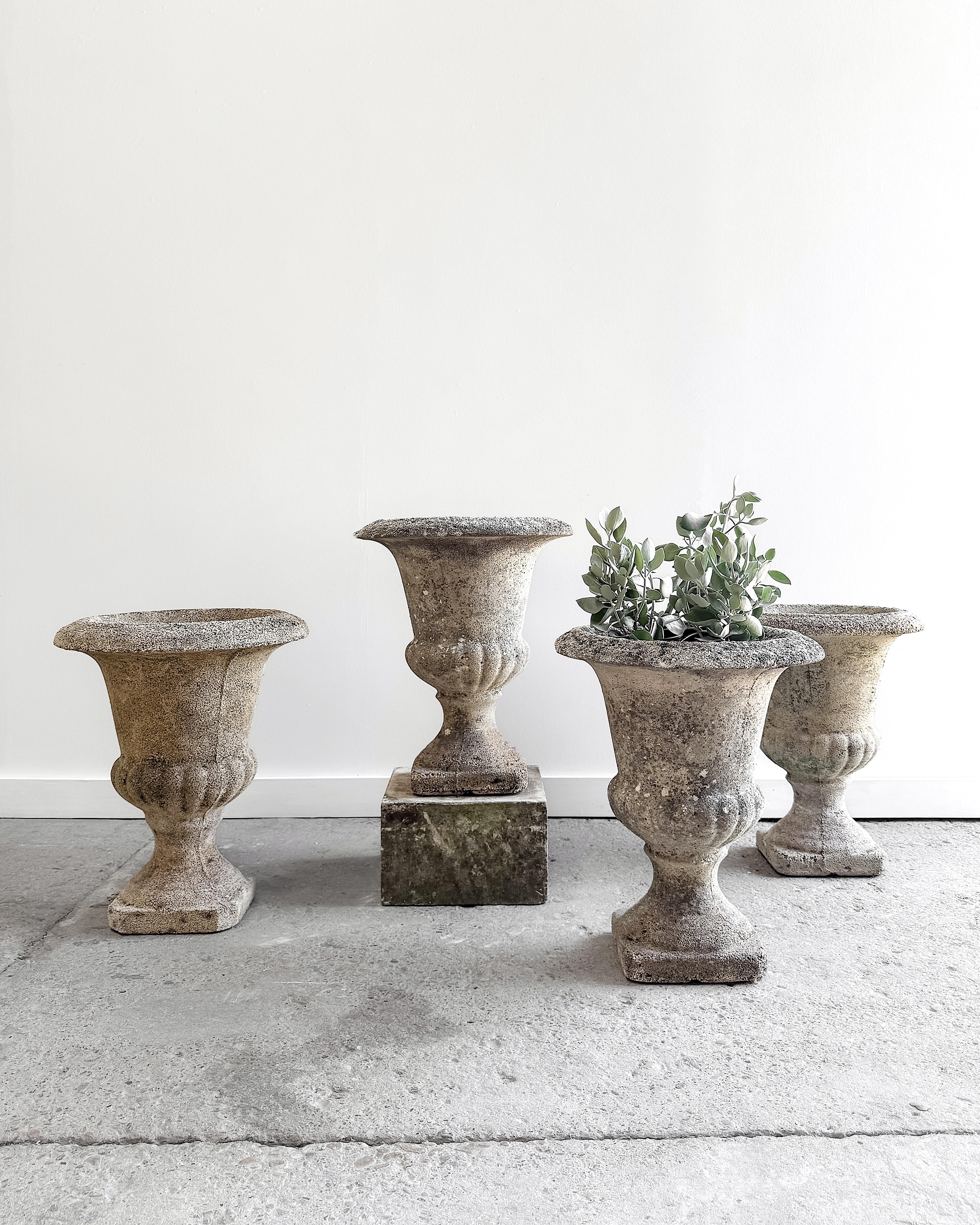 Two pairs of classic French urns that lend timeless form and texture to the garden or patio. Crafted from a cement composite with visible aggregate, they feature a gently weathered surface that speaks to decades spent outdoors. 

Their elegant