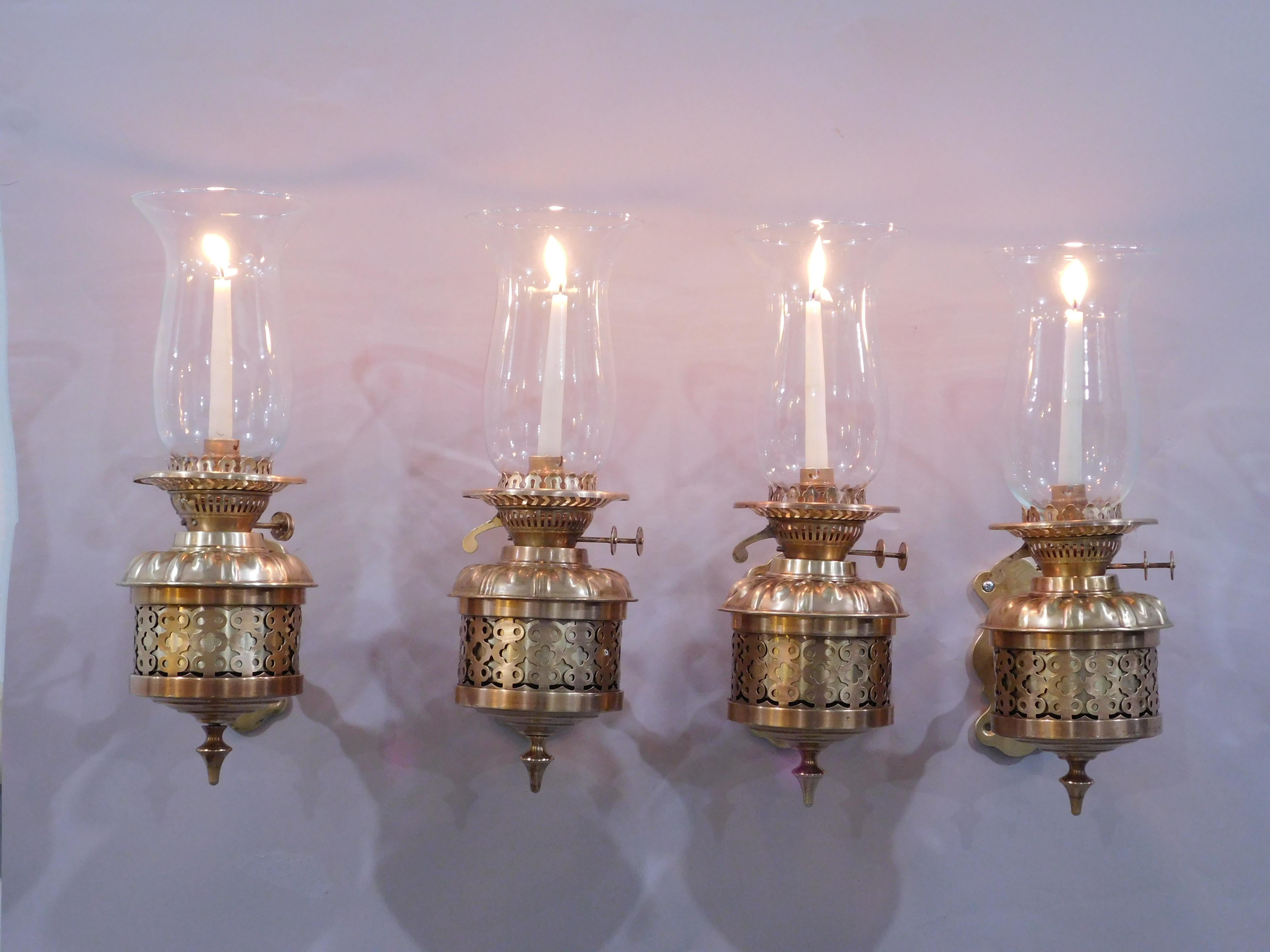 Unique set of 4 English Brass and Bronze Candle Hurricane Lantern Sconces. Hand hammered brass repoussé wall lamps, circular brass oil font body with pierced fret quatrefoil, four-leaf clover design which is often found in Gothic architecture