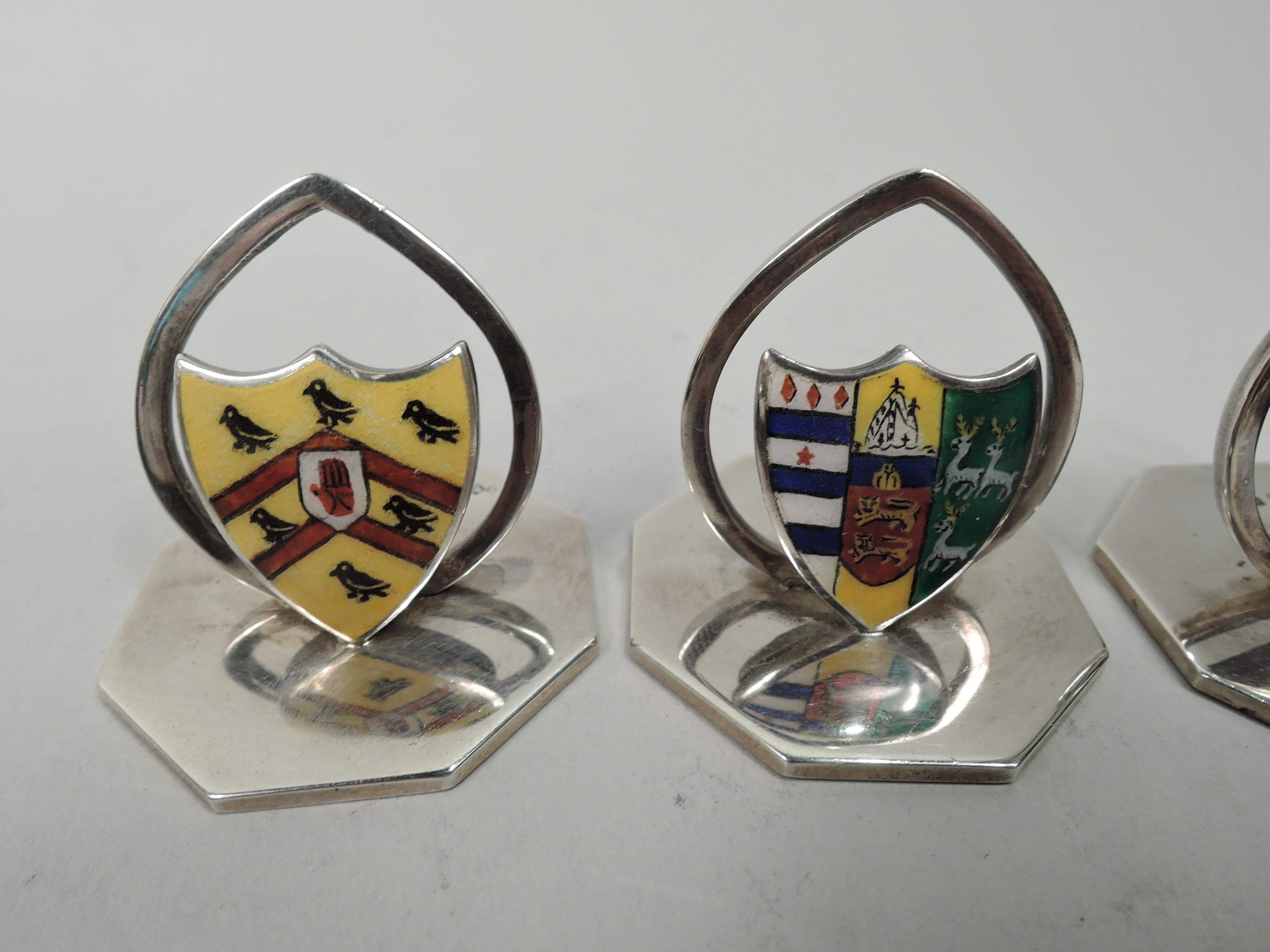 Set of 4 Edwardian sterling silver and enamel place card holders. Made by James William Benson in Birmingham, 1901 to 1902. Each: Enameled coat of arms and open oval clip mounted to flat octagonal base. Two each in two coats of arms. In