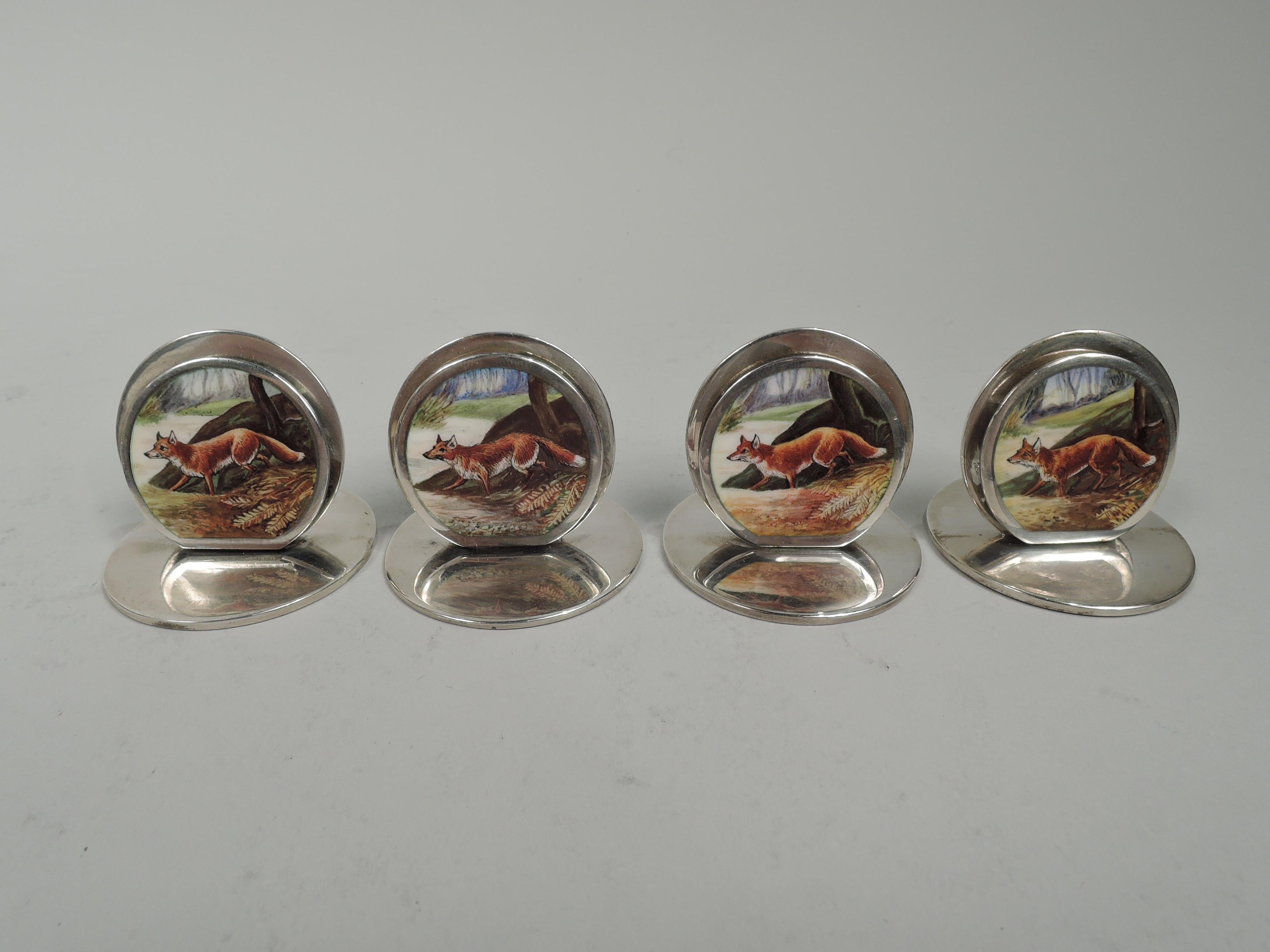Set of 4 Edwardian sterling silver place card holders. Made by Sampson Mordan & Co. Ltd. in Chester, 1904-6. Each: Two flat discs mounted to flat and circular base. Front disc smaller and enameled with fox loping through forest. In leather-bound