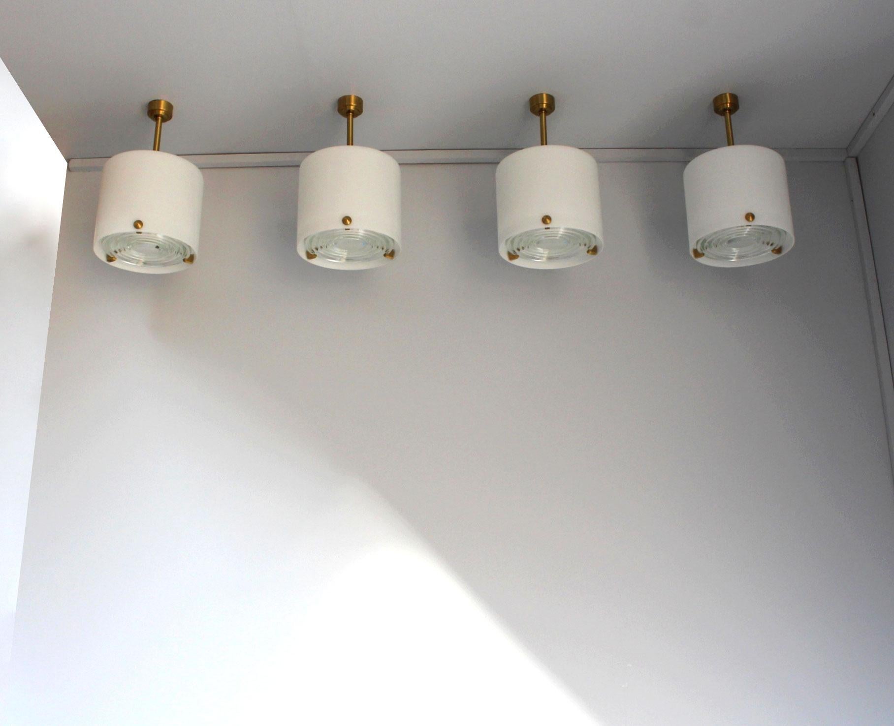 Jean Perzel: A set of four fine French midcentury cylinder-shaped chandeliers/pendants with a white satin laminated glass shade, a bronze canopy, stem and 3 studs that support a prismatic glass lens.