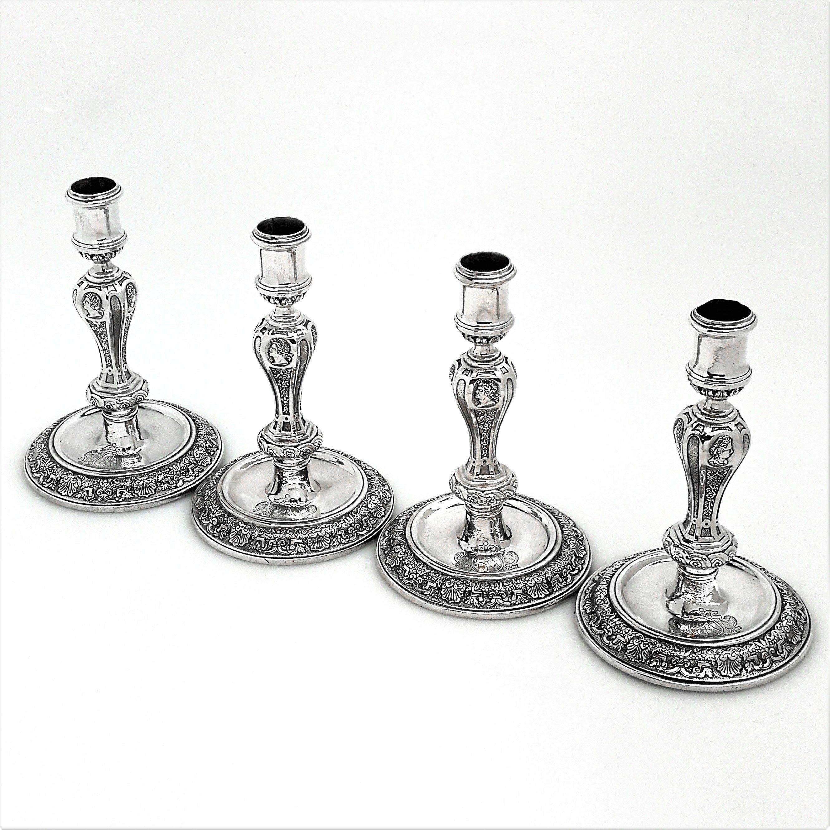 A magnificent set of four George I Sterling Silver Candlesticks. These Candlesticks feature round bases with a shell and foliage border surrounding sunken wells. The Candlesticks have shaped octagonal columns with portraits on the shoulders. The