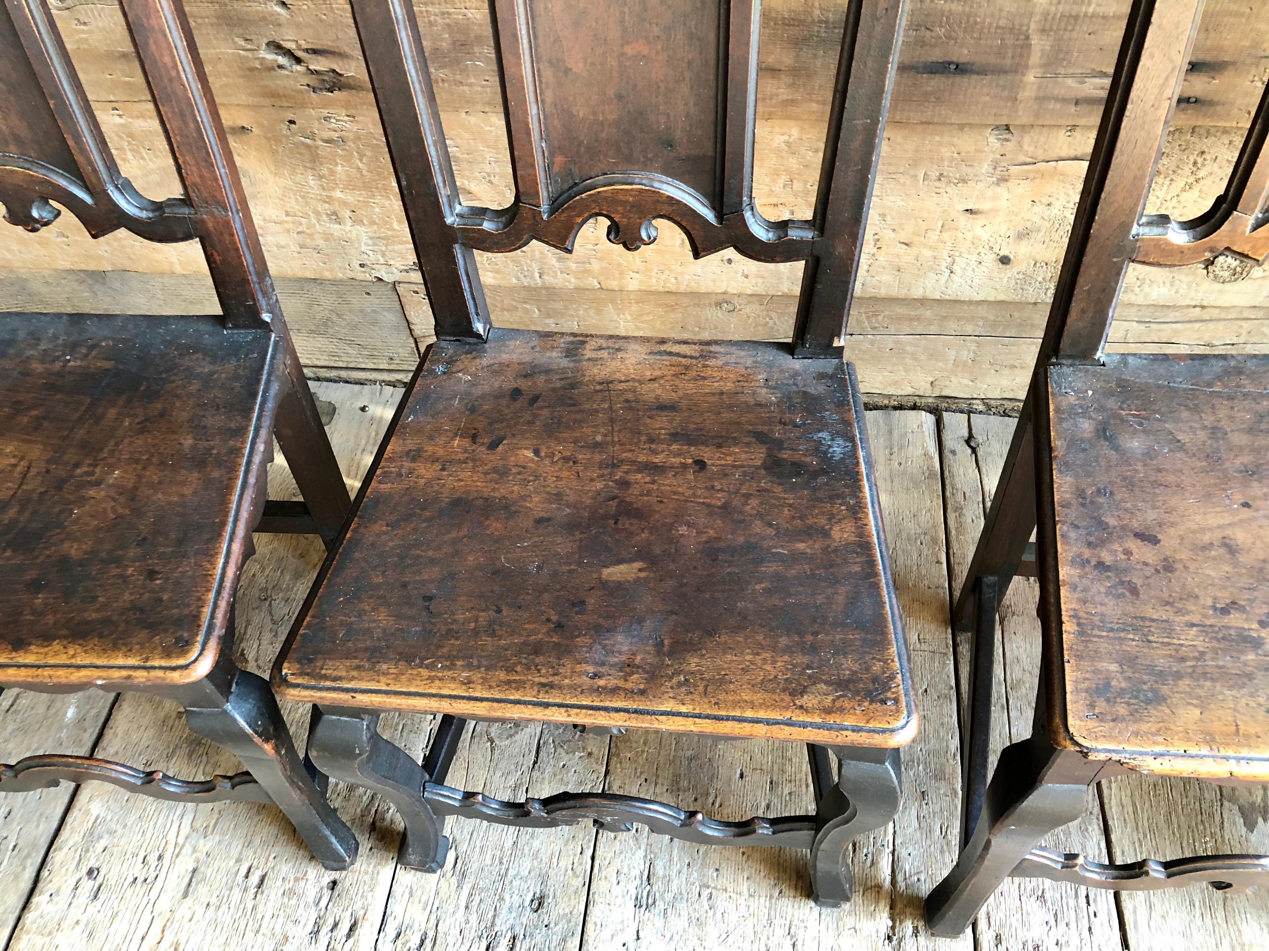 A set of 4 Italian 18th century hall chairs with Gothic elements, in walnut, with wood seats, a carved back panel all on cabriole legs, circa 1780.