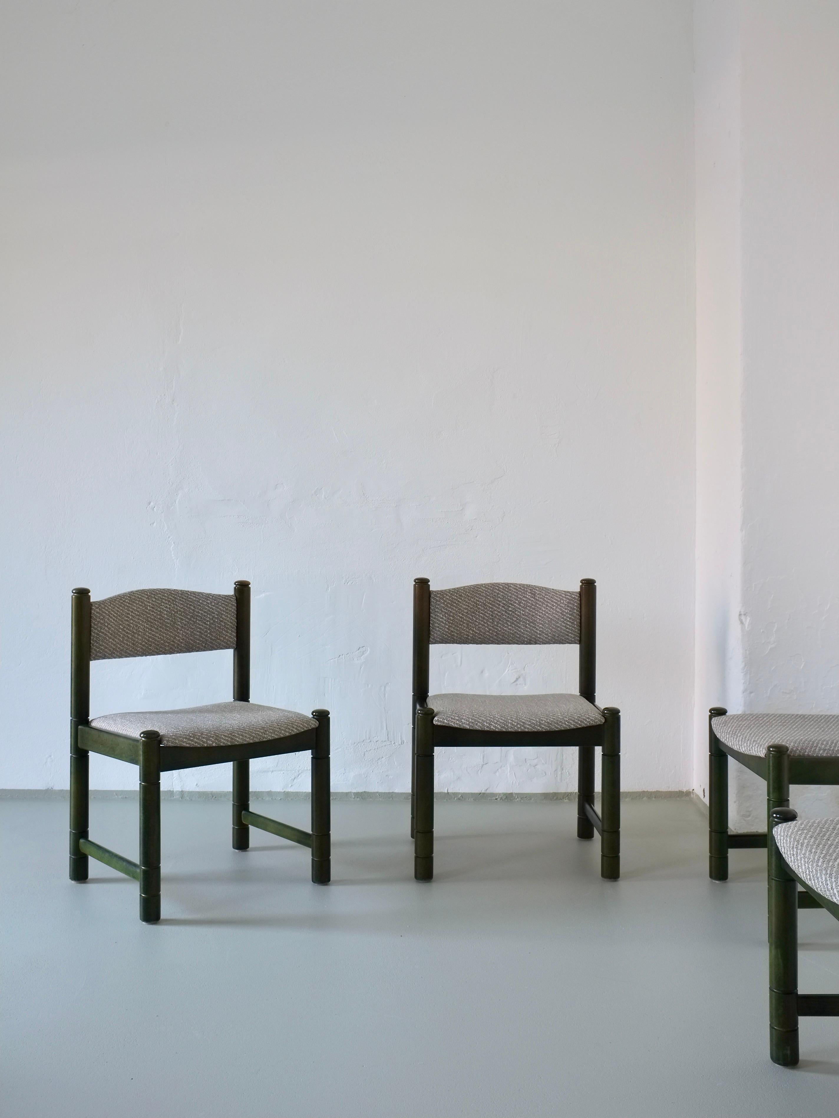 Un ensemble de quatre chaises en bois teinté en vert avec des sièges et des dossiers rembourrés en bleu grisâtre. Ces chaises sont lourdes et robustes et offrent un grand confort grâce à leur assise large et à leur dossier incurvé. 