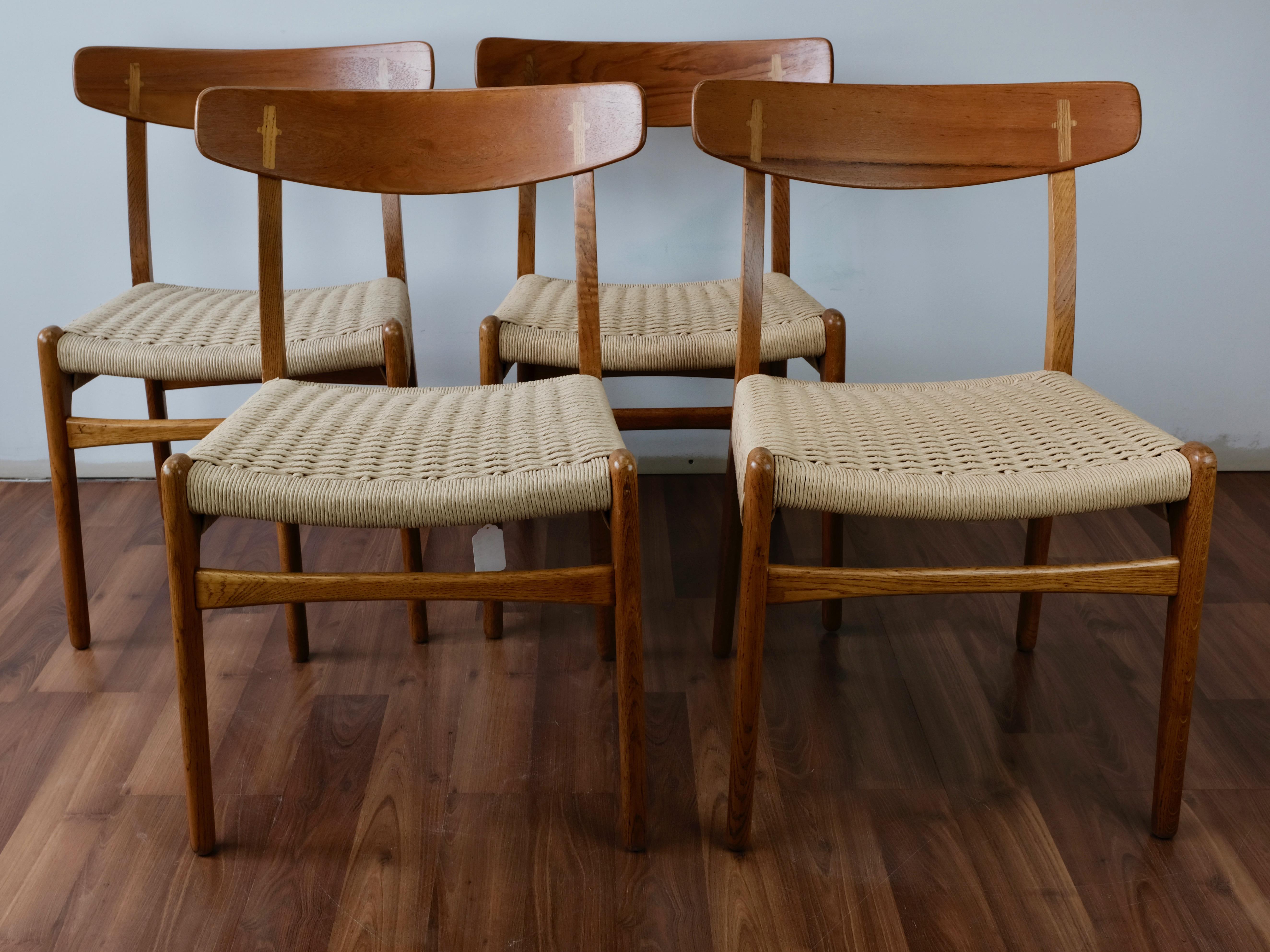 Set of 4 CH23 dining chairs designed by Hans Wegner and made in Denmark by Carl Hansen & Søn. 

The teak bent-lamination backrests feature distinctive cruciform cover caps in oak where the backs join the solid oak frames.

The double-woven paper