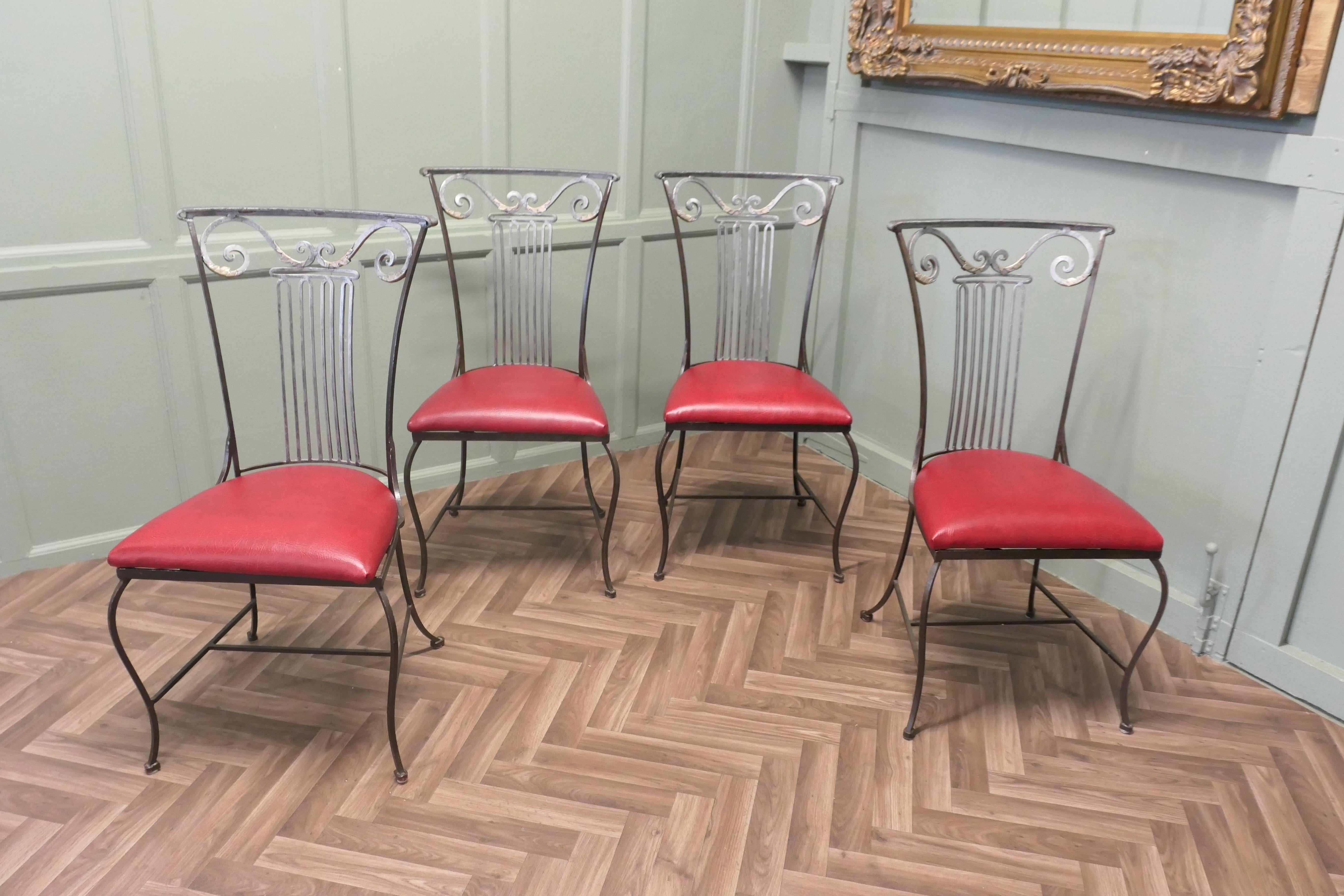 Ensemble de 4 chaises de salle à manger en fer à dossier haut

Les chaises ont de hauts dossiers légèrement incurvés qui s'évasent vers le haut où ils sont décorés d'un motif de lyre et de volutes. Elles ont des sièges en vinyle rouge nouvellement