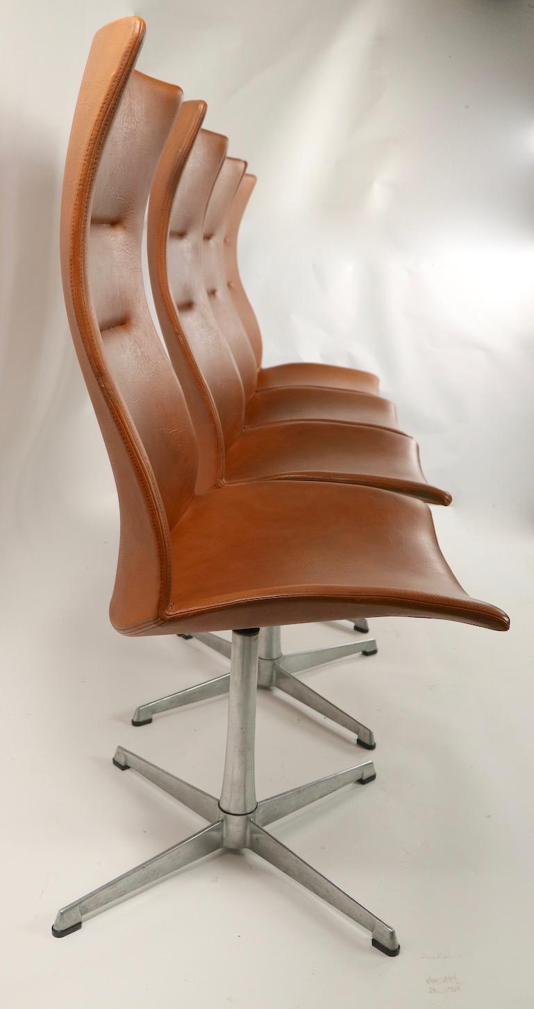 Rare set of 4 sculpted high back swivel dining chairs by Overman of Sweden. Extremely comfortable contoured back rests create an ergonomic seating experience. Cognac faux leather ( vinyl ) upholstered seats and backs, on cast aluminum star bases,