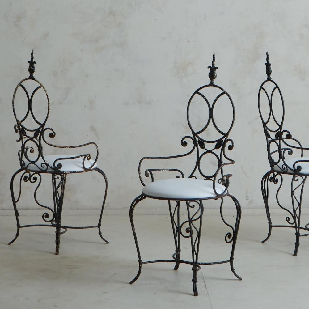 Ein Satz von 4 französischen Esszimmerstühlen im Vintage-Stil mit kunstvollen schmiedeeisernen Rahmen mit eleganten Schnörkeln, Blattmotiven und einer X-Support-Stange. Diese Stühle haben runde Rückenlehnen mit dekorativen Endstücken und stehen auf