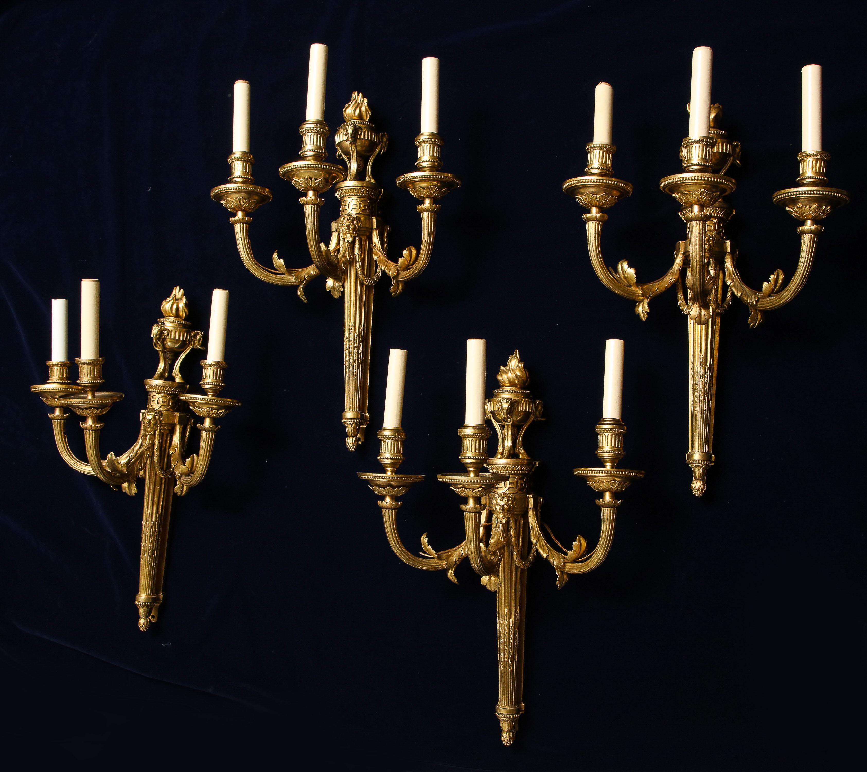A very unusual and quite rare set of four antique French Louis XVI period, three-light wall lights/appliqués, (sconces). Each having a Hercules mask to initialize each arm, with an ormolu urn and flame above all. The bronze finely cast and then