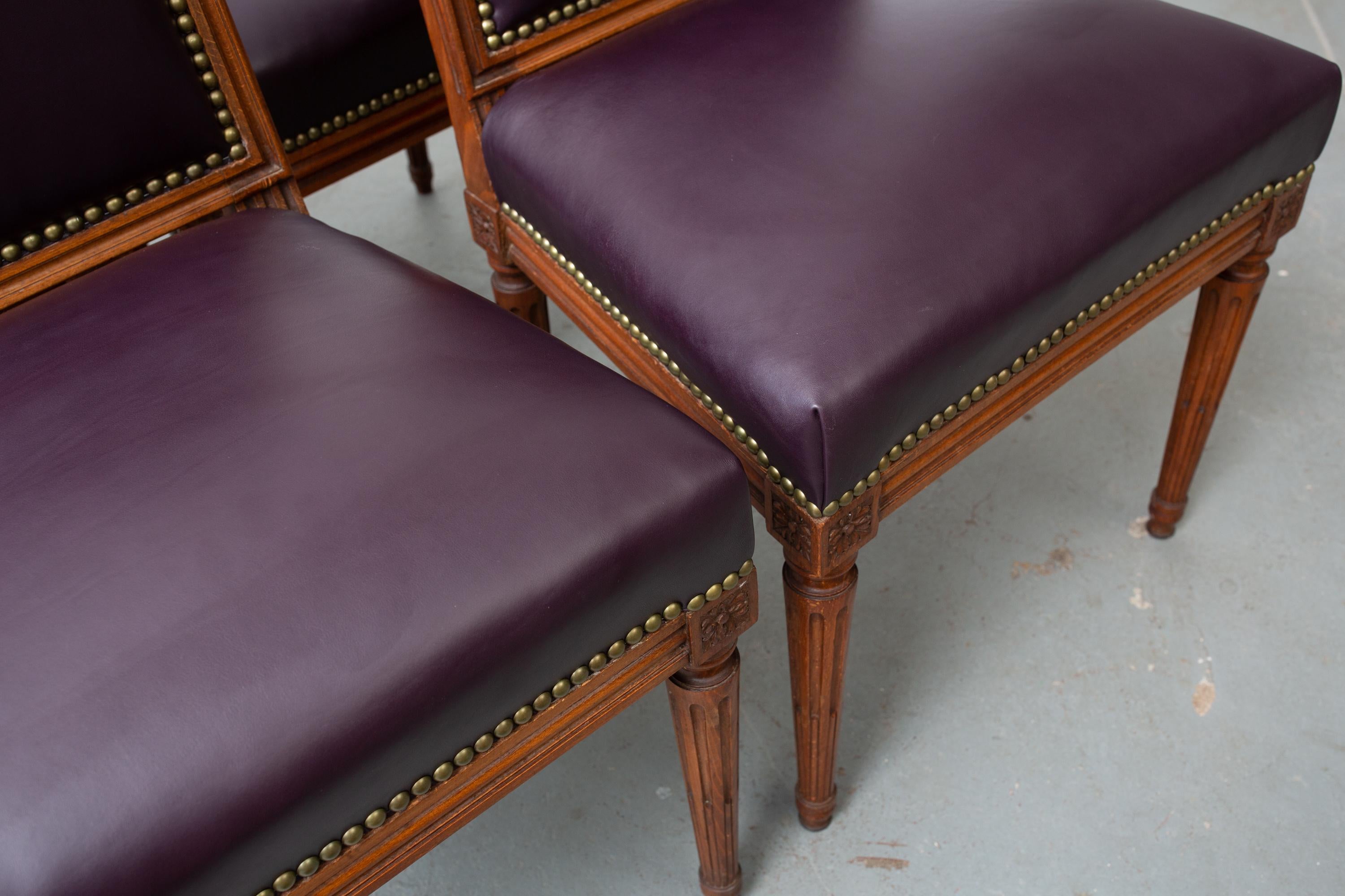 Set of four, 1940s Louis XVI style carved wood dining chairs newly upholstered in aubergine leather with nailhead trim. Tapered and fluted legs with carved flower detail to the corners. Wood is in great original condition. Very sturdy.