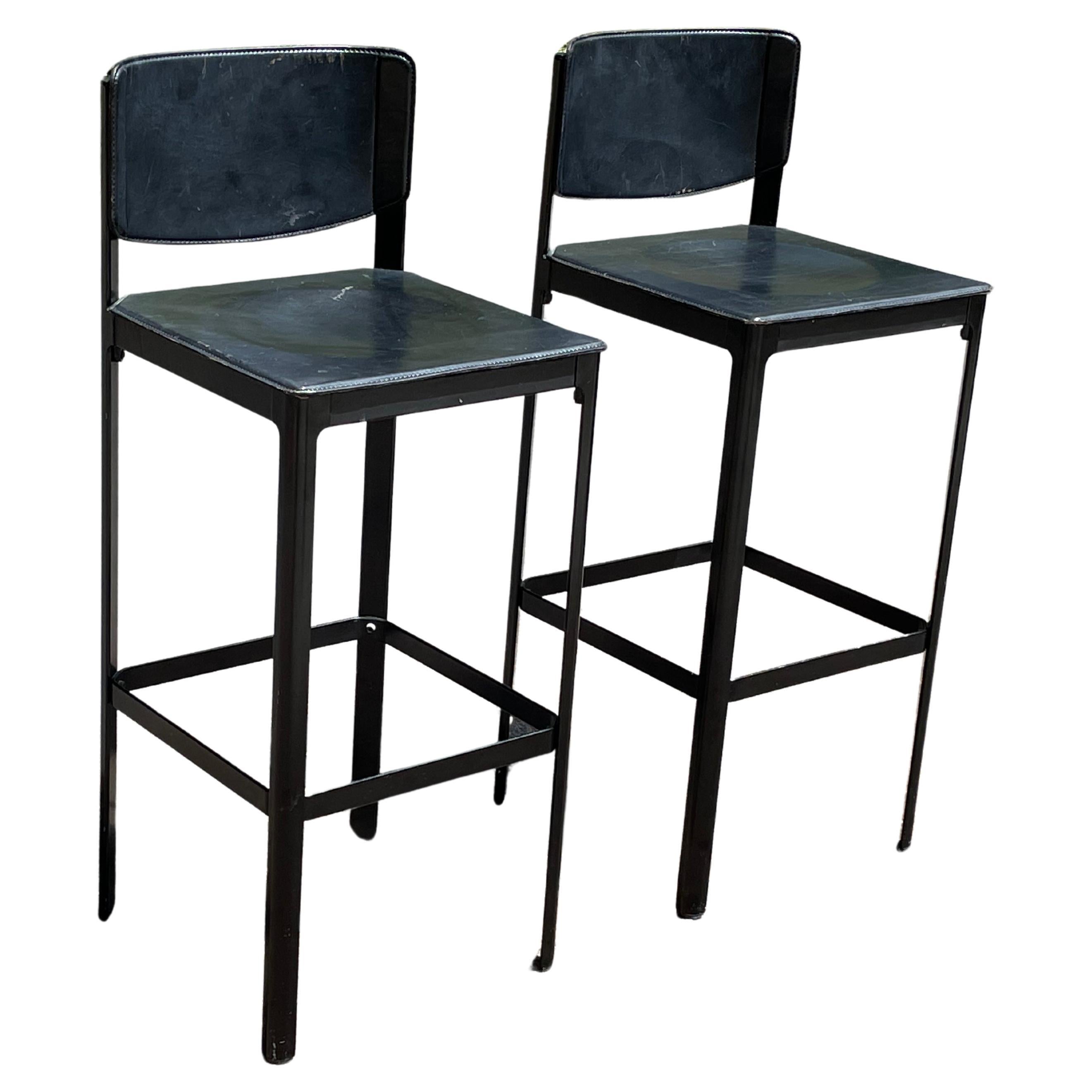 Mid-Century Matteo Grassi black leather bar stools. Italy. c.1980s.

Very cool design features a patinated black saddle leather wrapped atop a steel frame with stitched detailing. A black enameled square metal support bar connects all four legs and