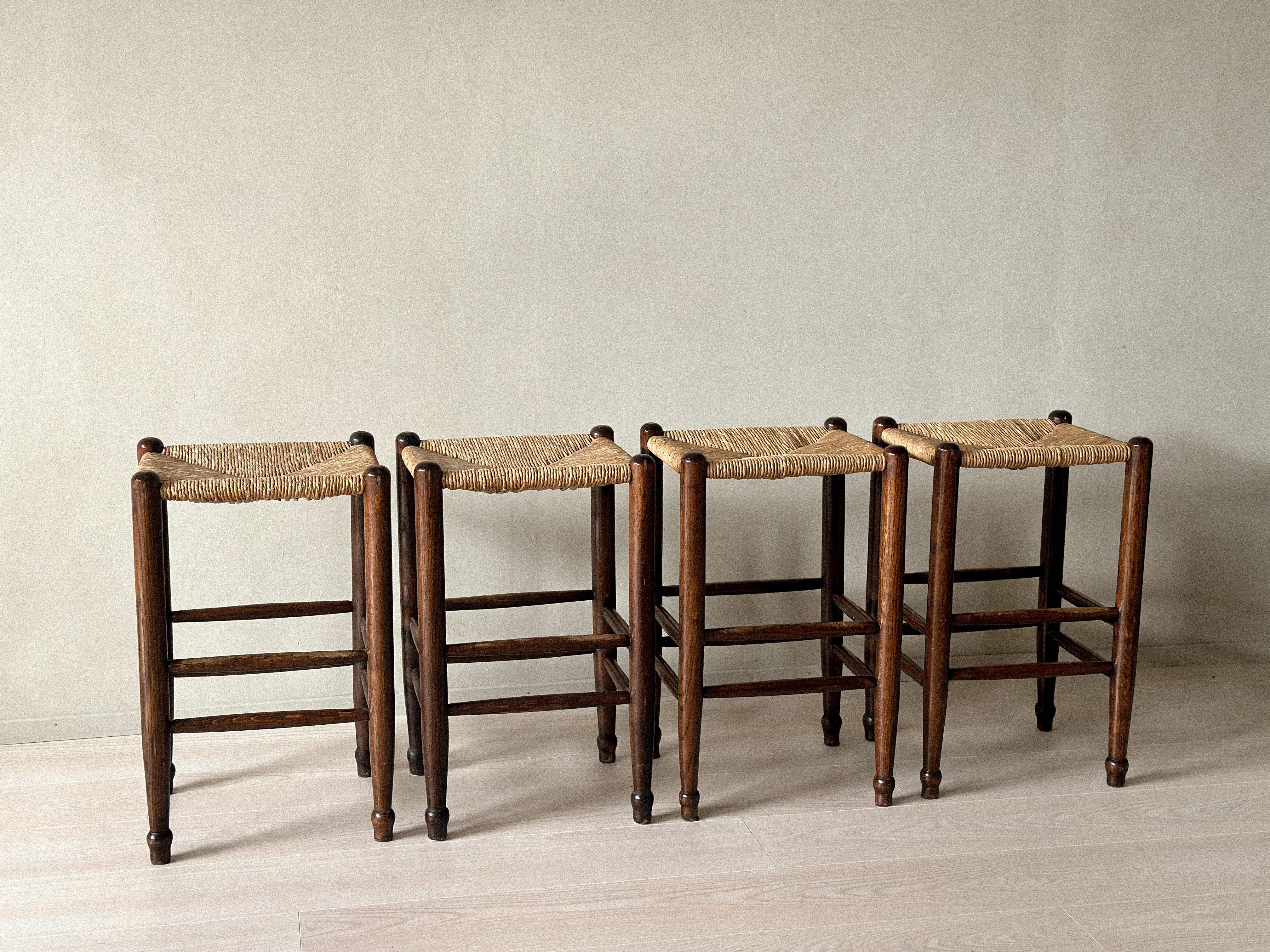 Satz von vier Barhockern aus der Mitte des Jahrhunderts mit Binsensitzen, Frankreich, um 1960. Rahmen aus Massivholz mit sichtbaren Tischlerarbeiten. Designer unbekannt.

Strukturell gesund. Leichte Risse an der Oberseite einiger Beine. Allgemeine