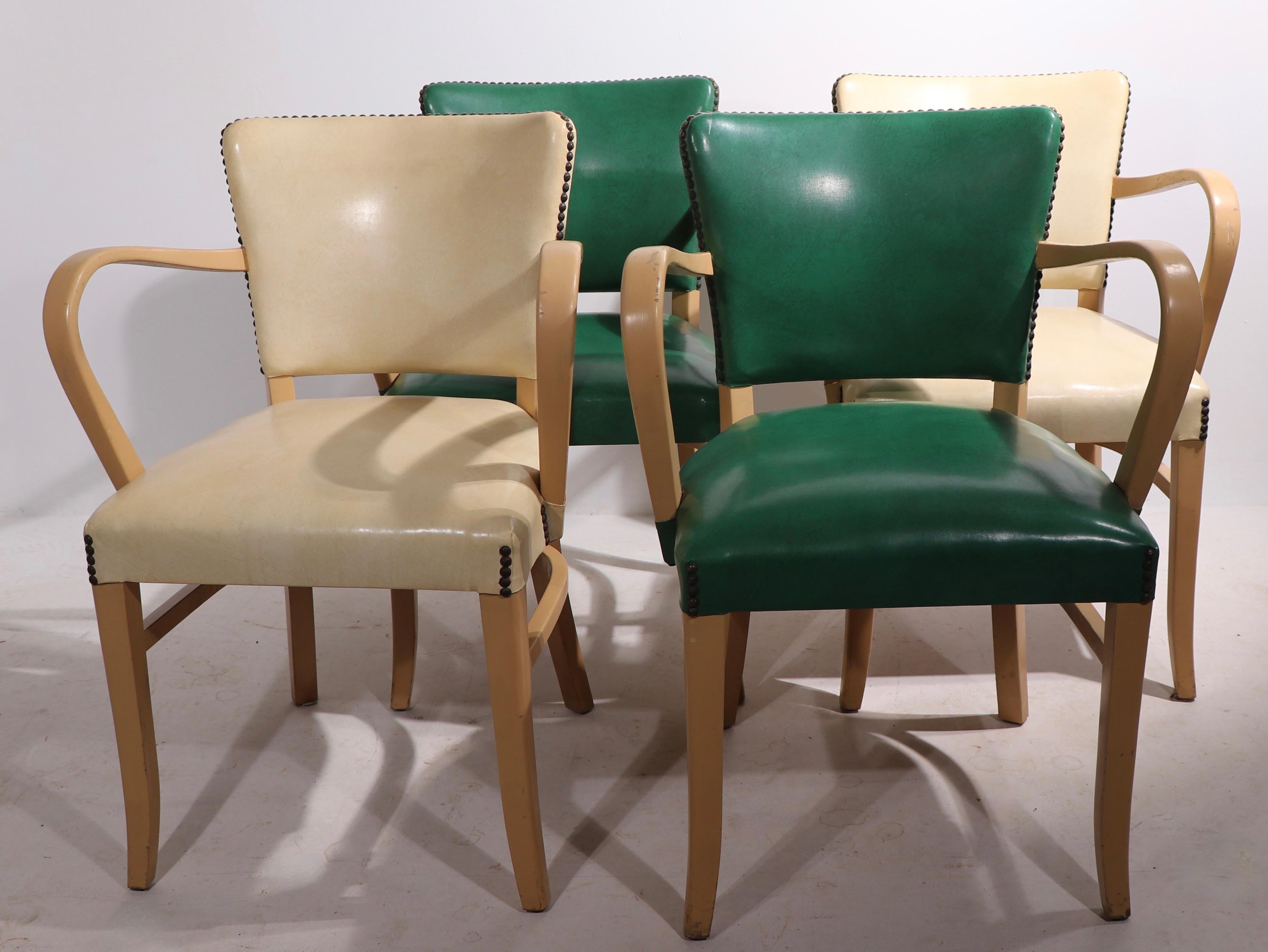 Chic stylish set of four mid century arm chairs having blonde wood frames, vinyl seats and backrests, and metal nail head stud trim. The theatrical and exaggerated arms create a dramatic profile, these chairs are pure style, a comfortable and ready